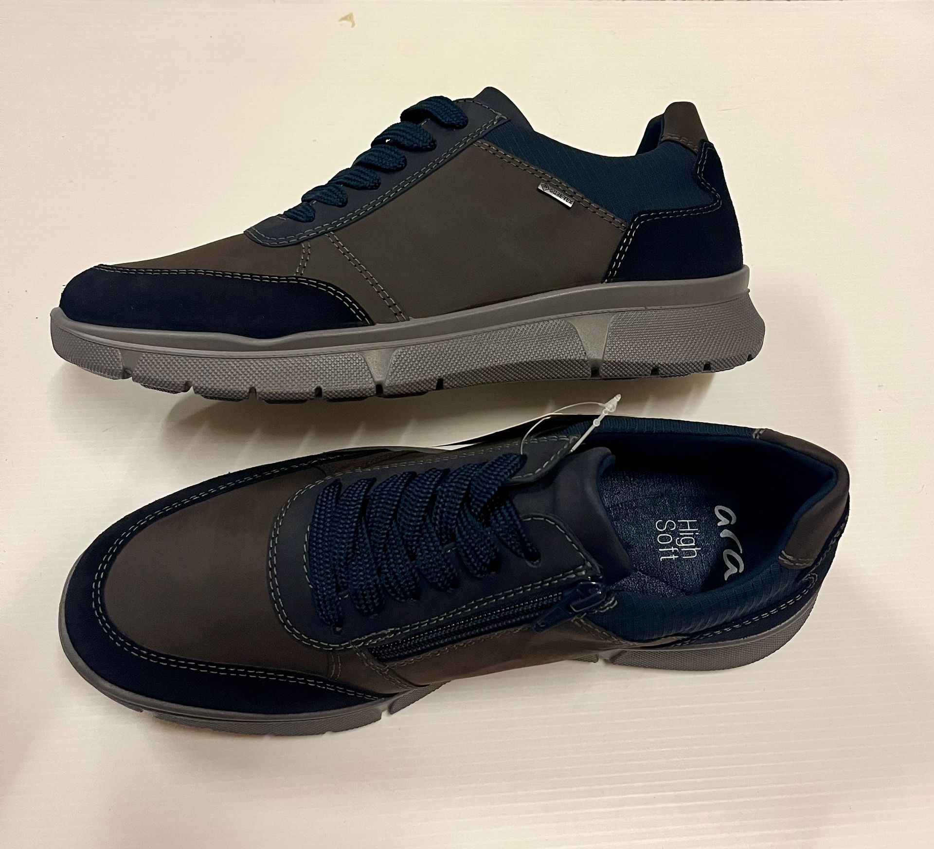 Due scarpe da ginnastica blu e grigie su una superficie bianca. Una vista laterale, l'altra dall'alto.