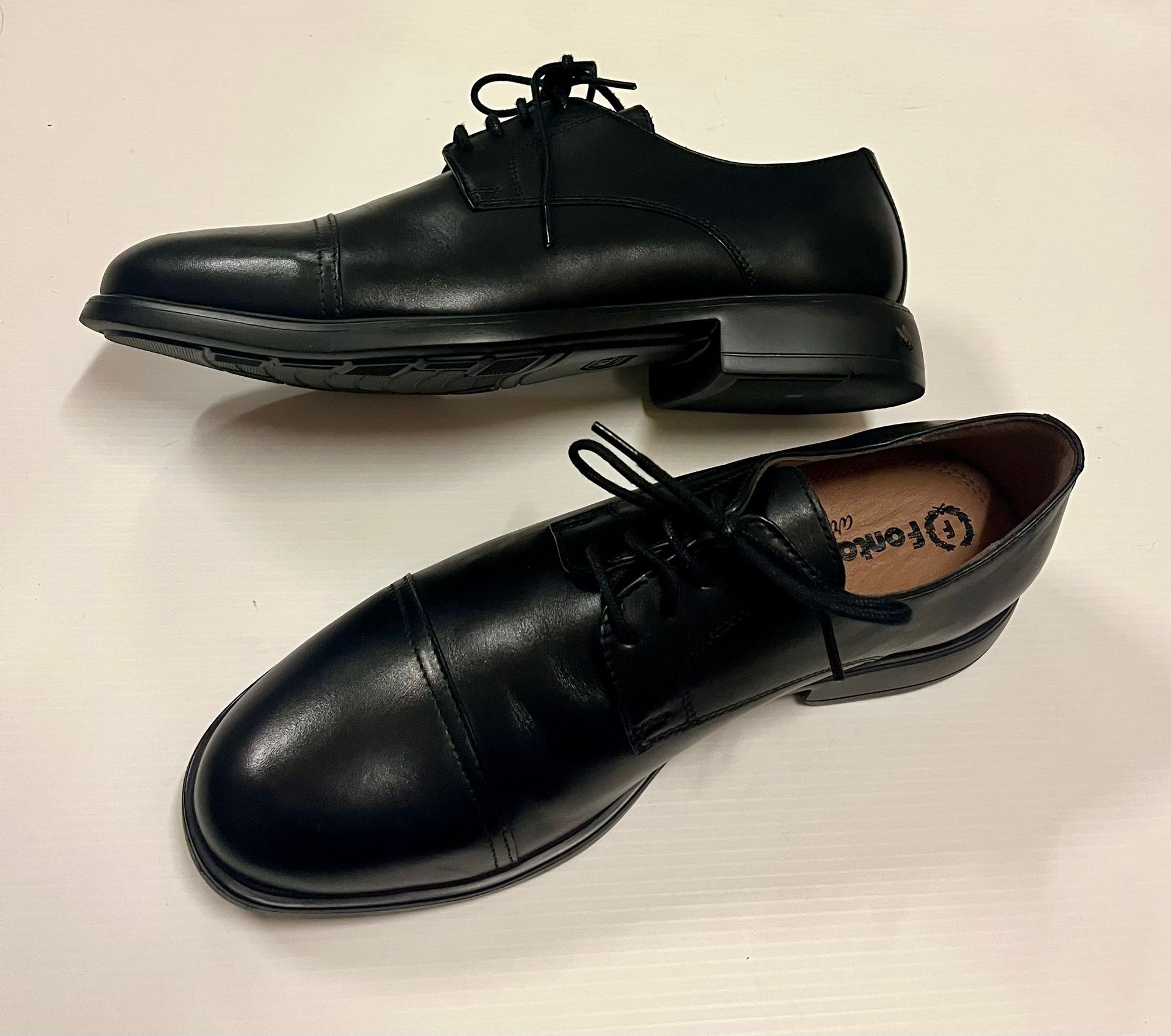 Due scarpe eleganti in pelle nera su una superficie bianca, una delle quali leggermente rialzata.