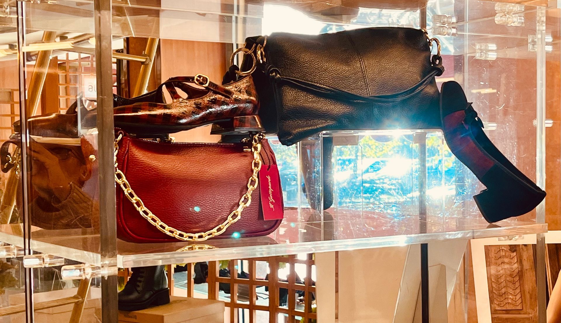 Vetrina con borse e una scarpa. Toni del rosso, del nero e dell'oro. Luce intensa sullo sfondo.