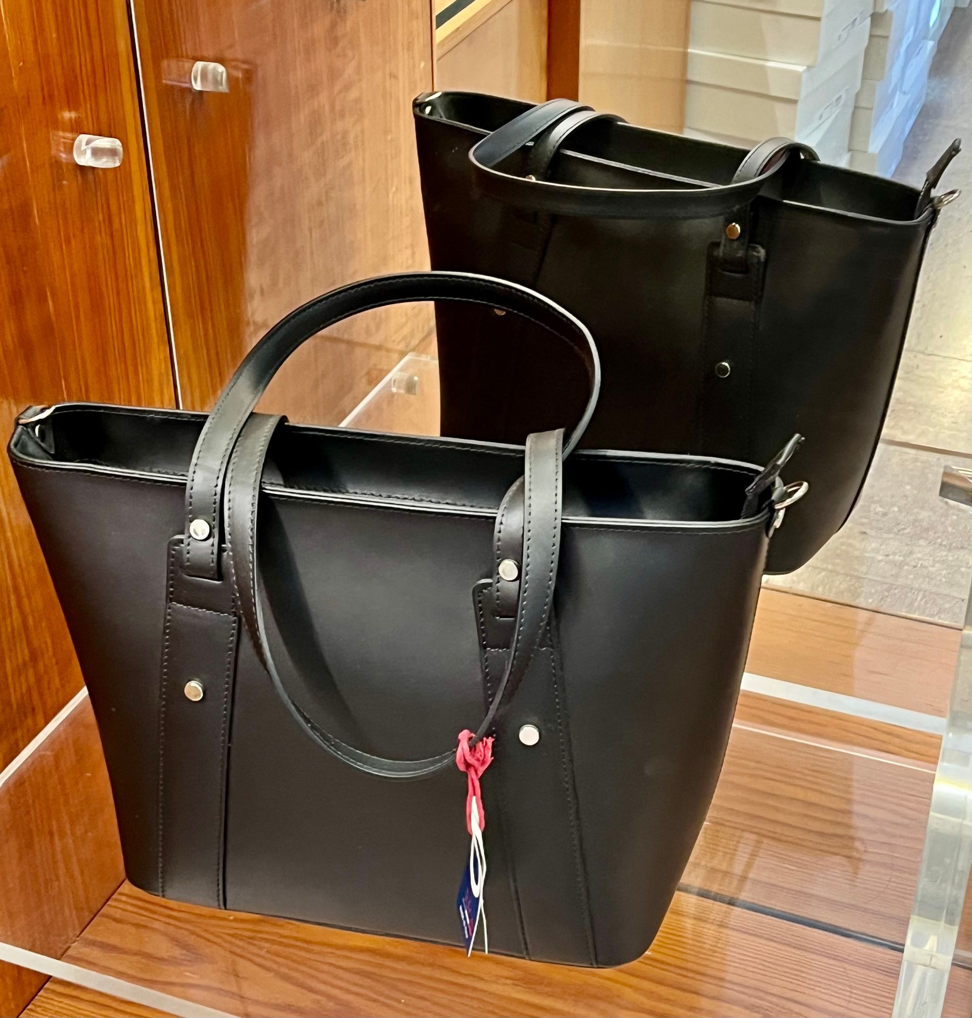 Due borse tote nere con manici, esposte su uno scaffale di vetro in un negozio.