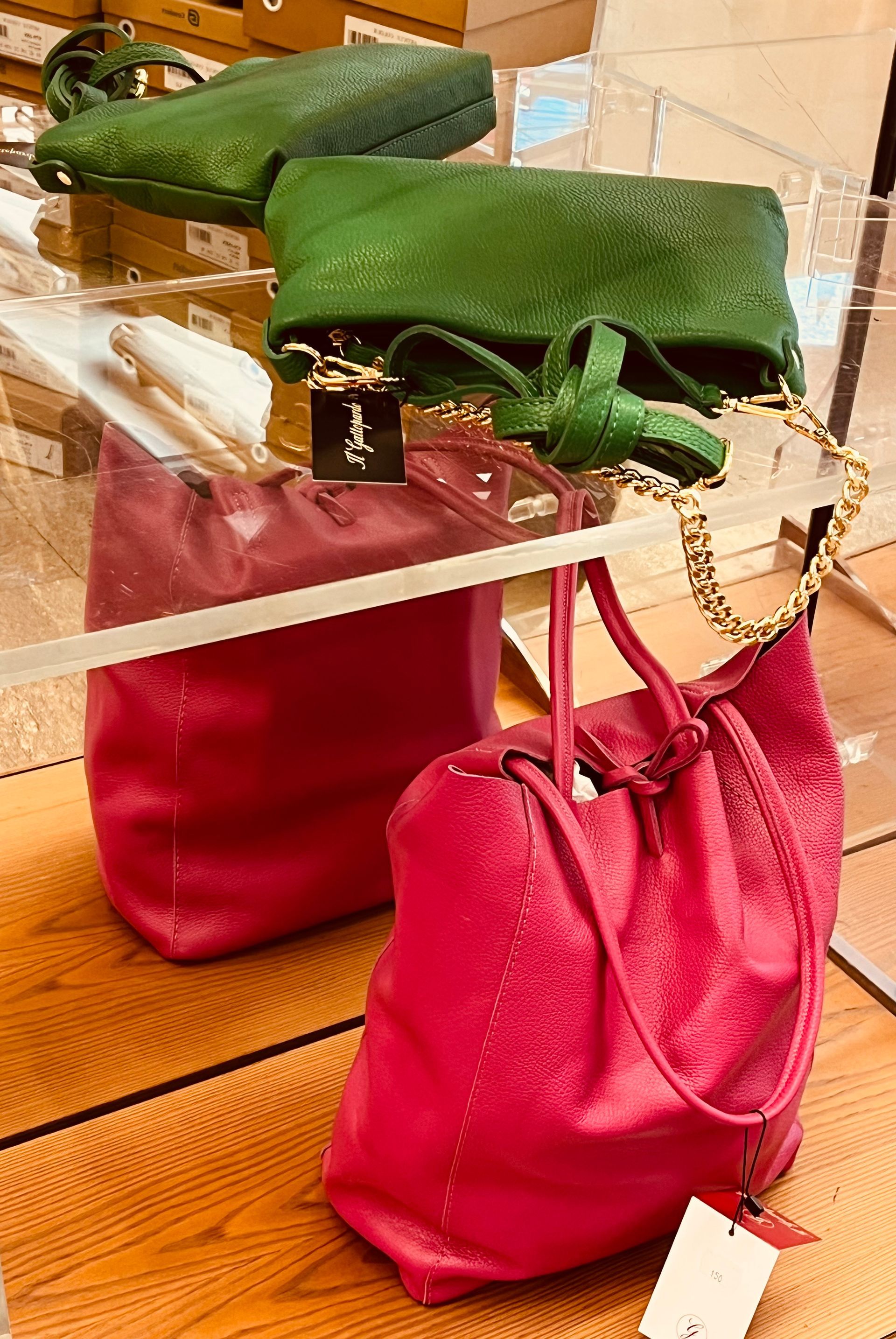 Esposizione di diverse borse in pelle nelle tonalità del verde e del rosso.