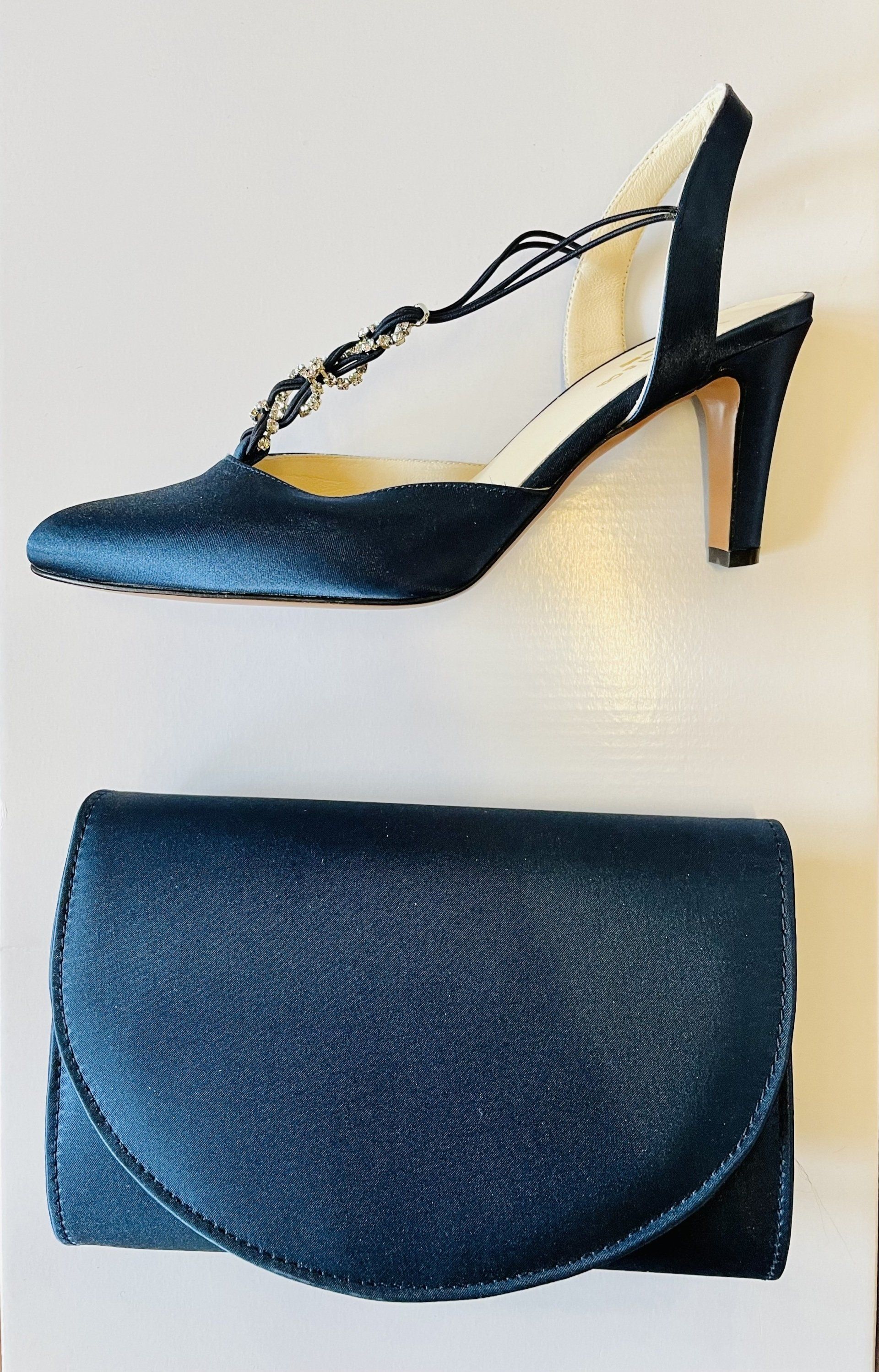 Scarpa elegante blu navy e pochette coordinata su una superficie bianca.