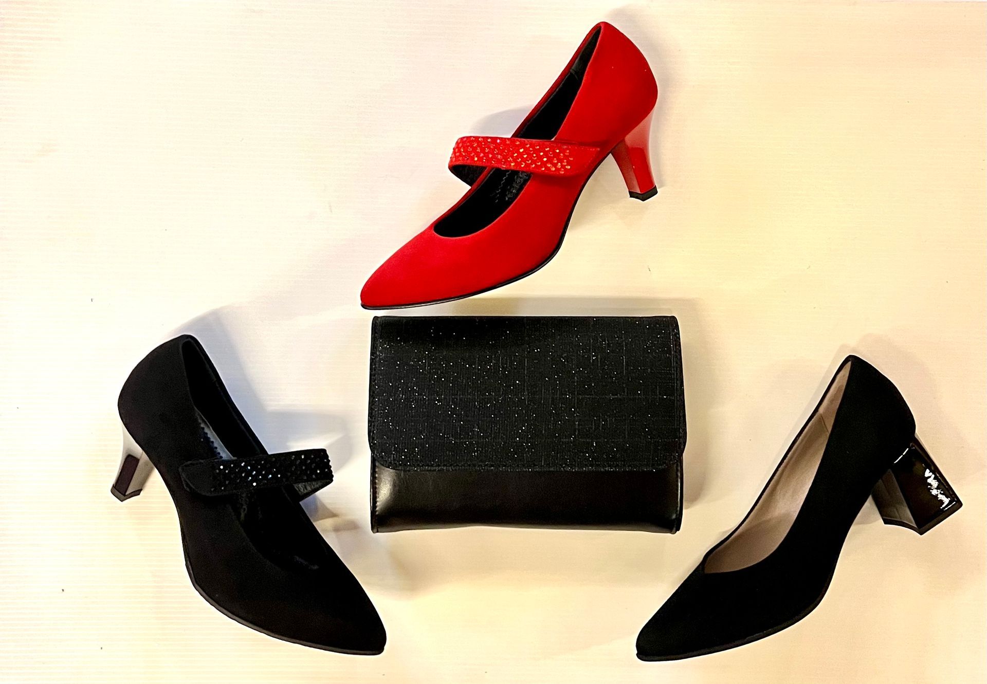 Scarpe col tacco rosse e nere e una pochette nera, disposte su una superficie bianca.