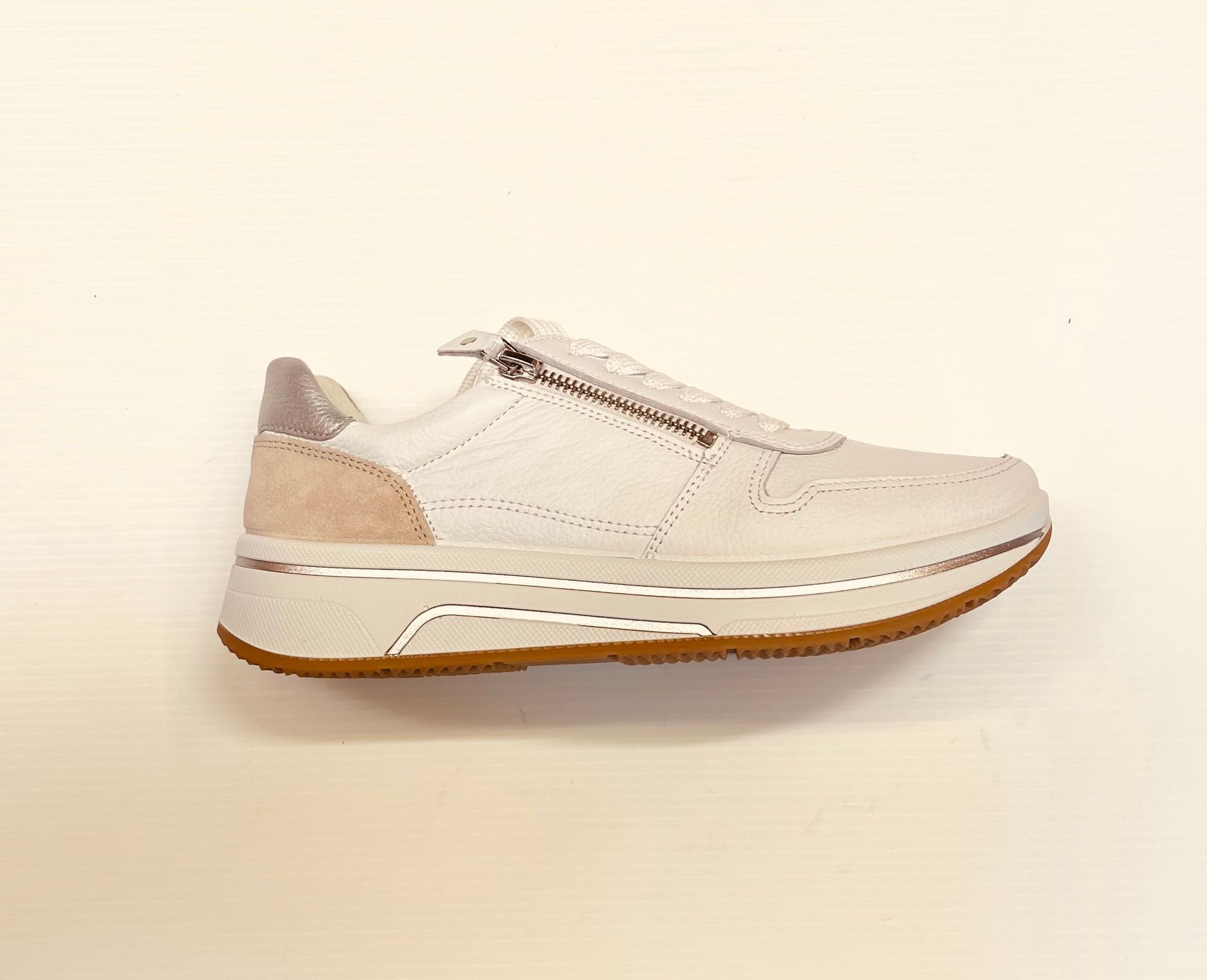 Sneaker color crema con chiusura a cerniera e suola marrone, su sfondo chiaro.