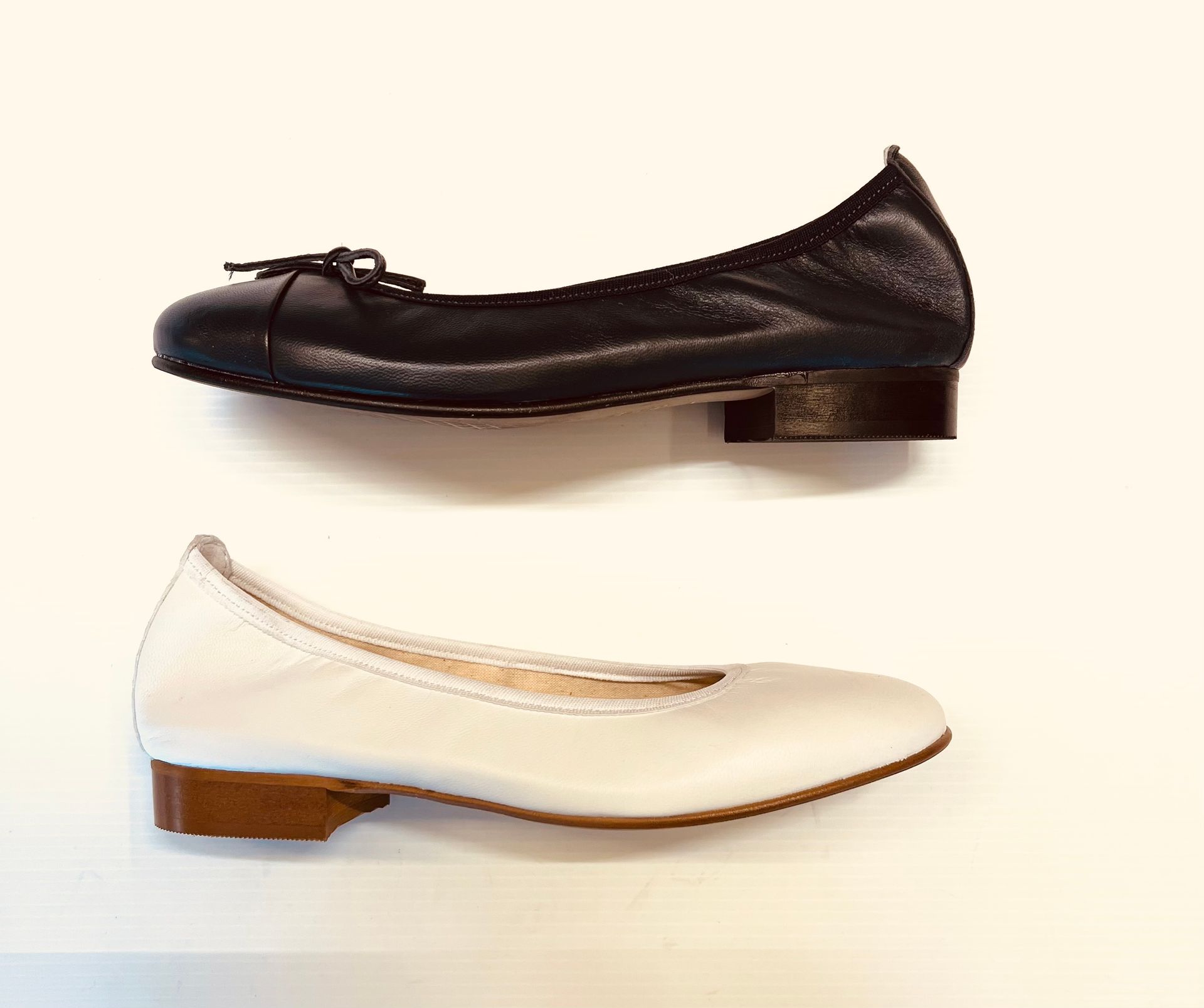 Ballerine in pelle bianca e nera, una accanto all'altra, su una superficie bianca.