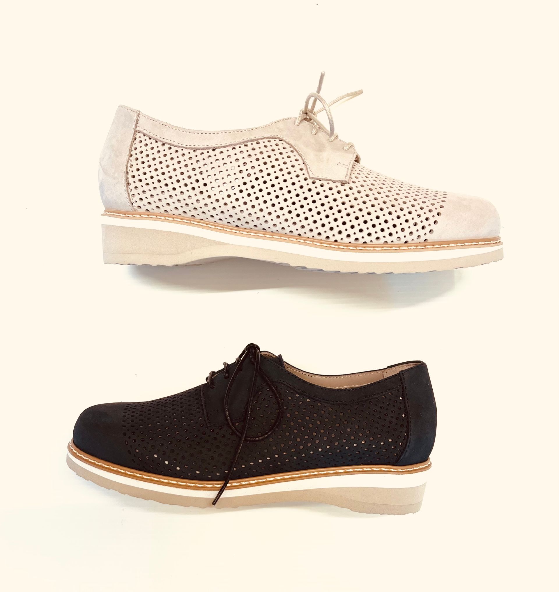 Due scarpe Oxford in pelle traforata, una beige e una nera, con suola e lacci bianchi.