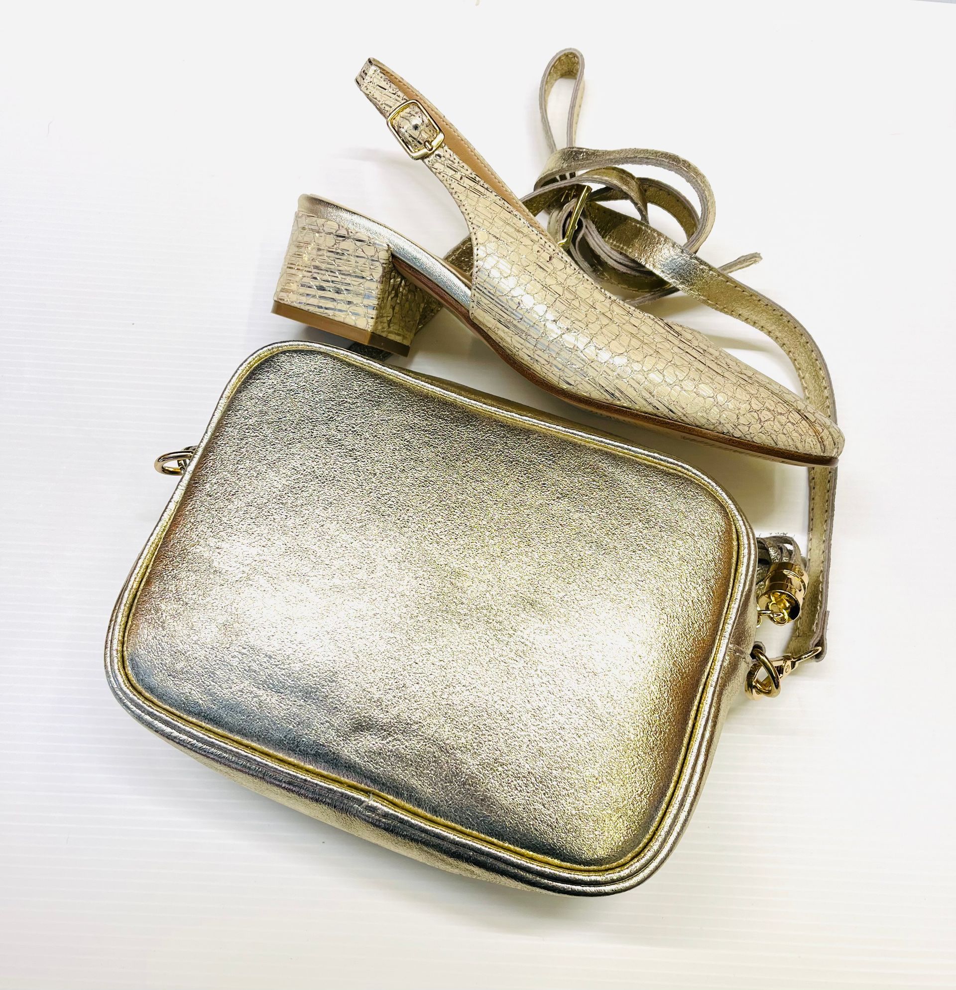 Scarpe con tacco slingback glitterate dorate e borsa a tracolla coordinata su una superficie bianca.