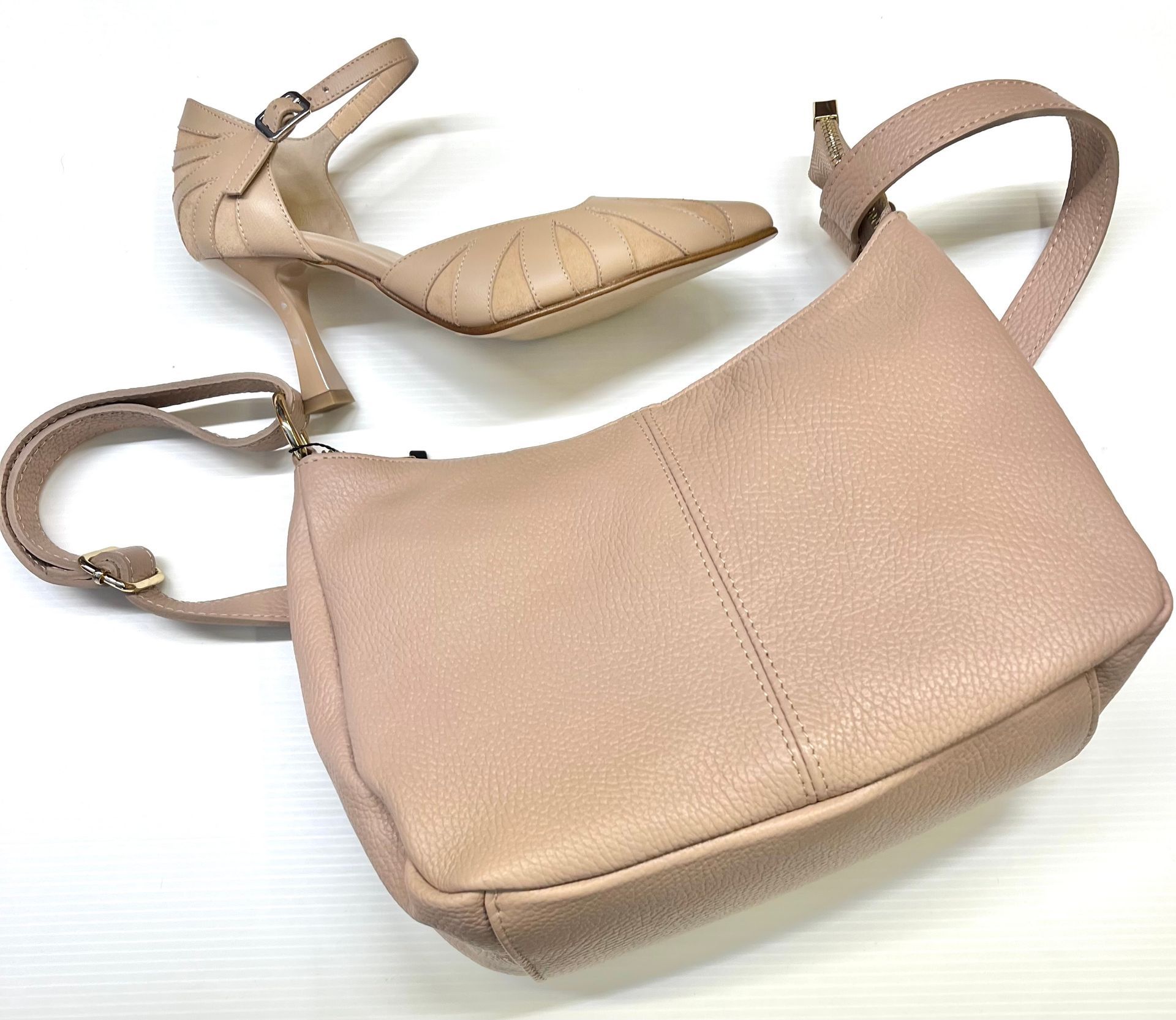 Borsa beige e scarpa con tacco alto su una superficie bianca.