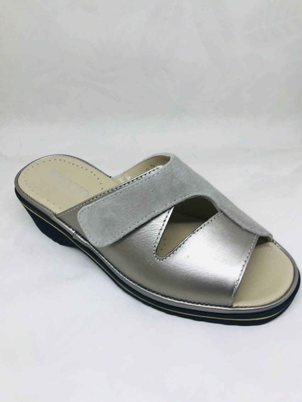 Sandalo slip-on color argento con soletta interna chiara e cinturino in pelle scamosciata grigia sul piede.