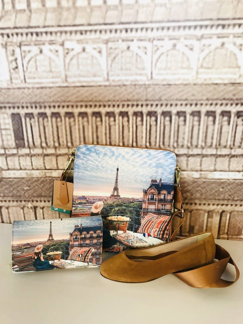 Ballerine marroni, pochette e biglietto d'auguri a tema parigino, sullo sfondo la facciata di un edificio.