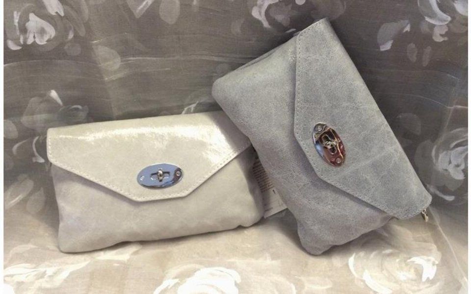 Due pochette in pelle scamosciata grigia, ciascuna con patta e chiusura decorativa, su una superficie fantasia.