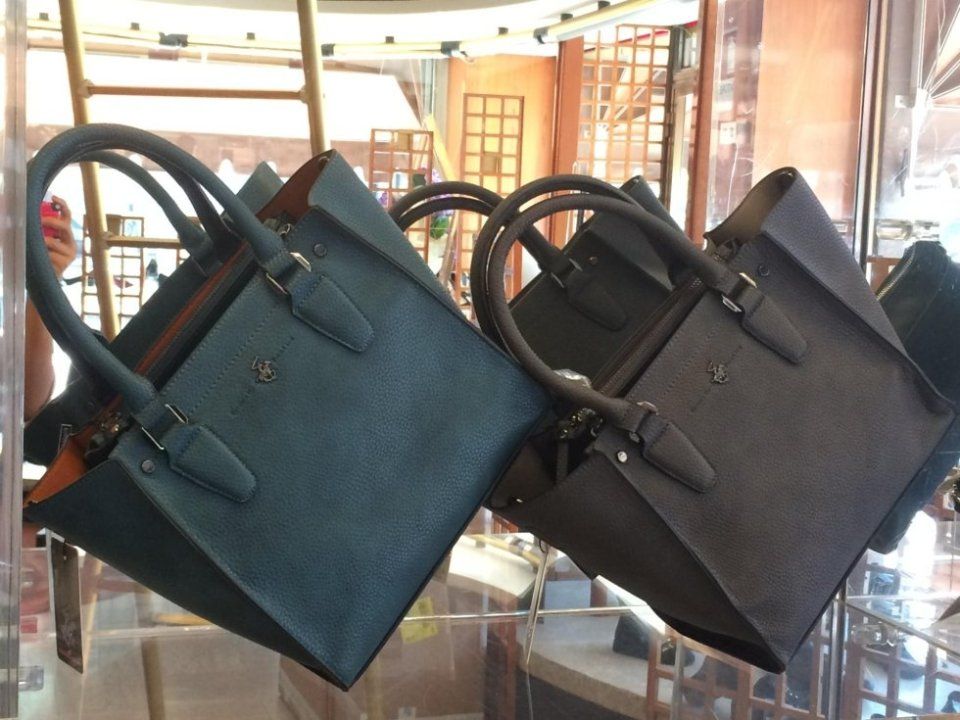Due borse in pelle con manici esposte nella vetrina di un negozio: una è color verde acqua e l'altra grigio scuro.