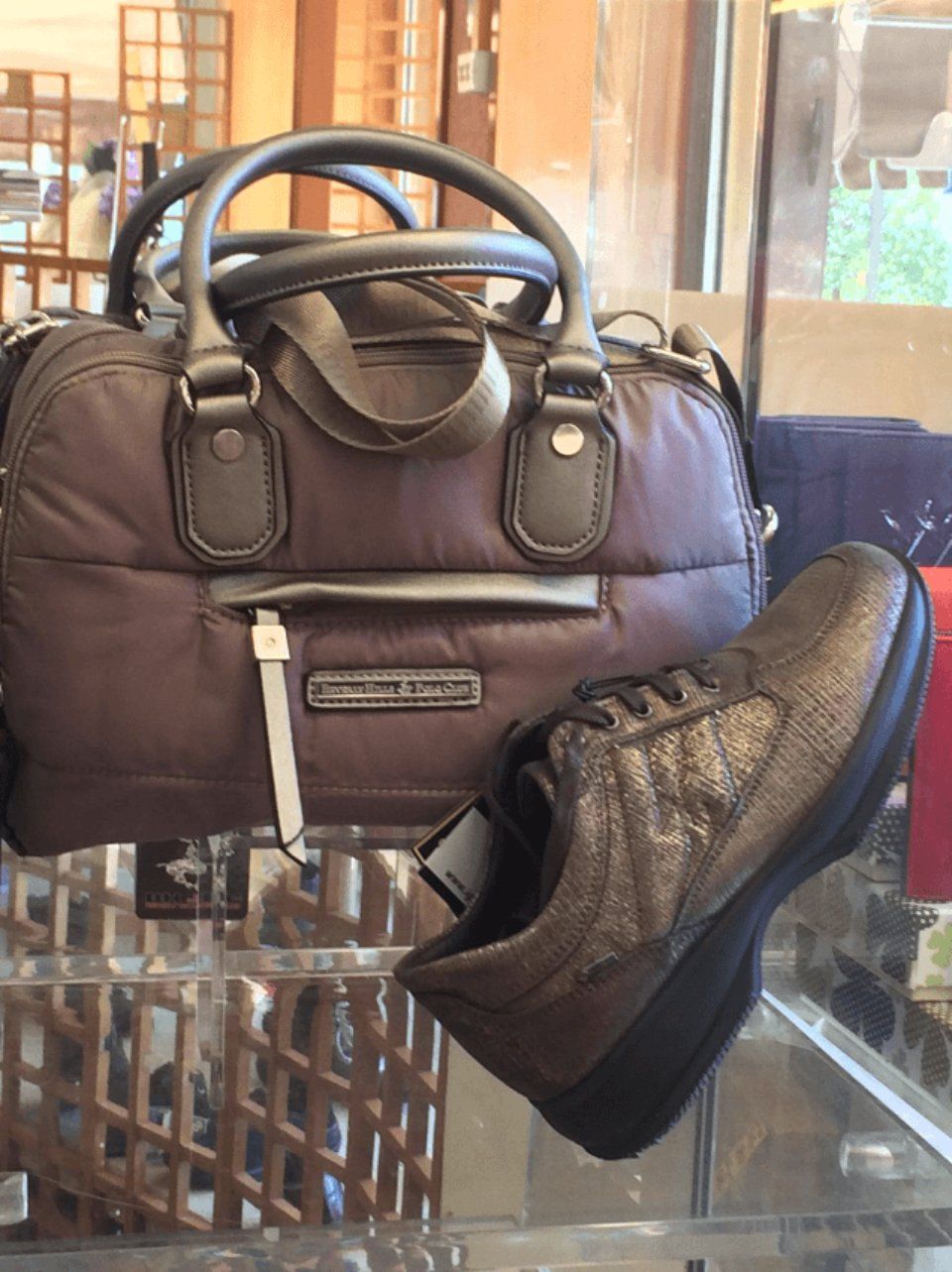 Borsa marrone e scarpe da ginnastica metallizzate su uno scaffale di vetro in un espositore di un negozio.