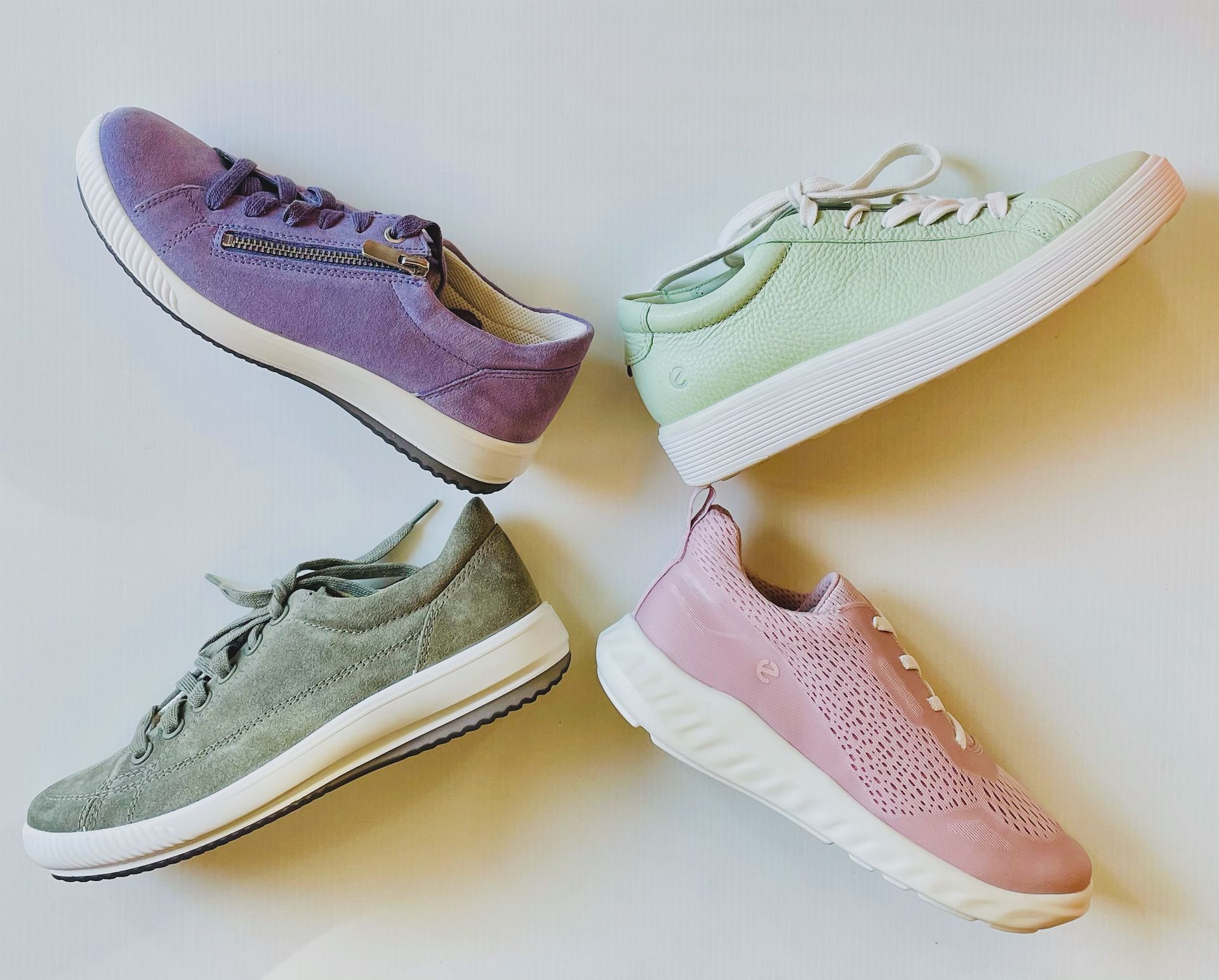 Quattro scarpe da ginnastica colorate: viola, verde, grigio e rosa, disposte su una superficie bianca.