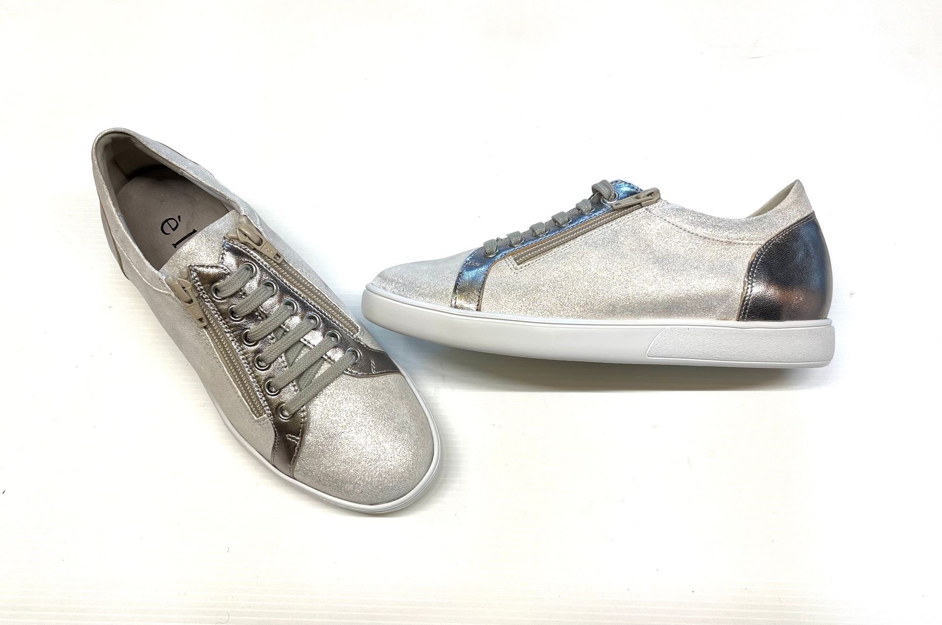 Sneakers glitterate argentate con suola bianca su una superficie bianca.