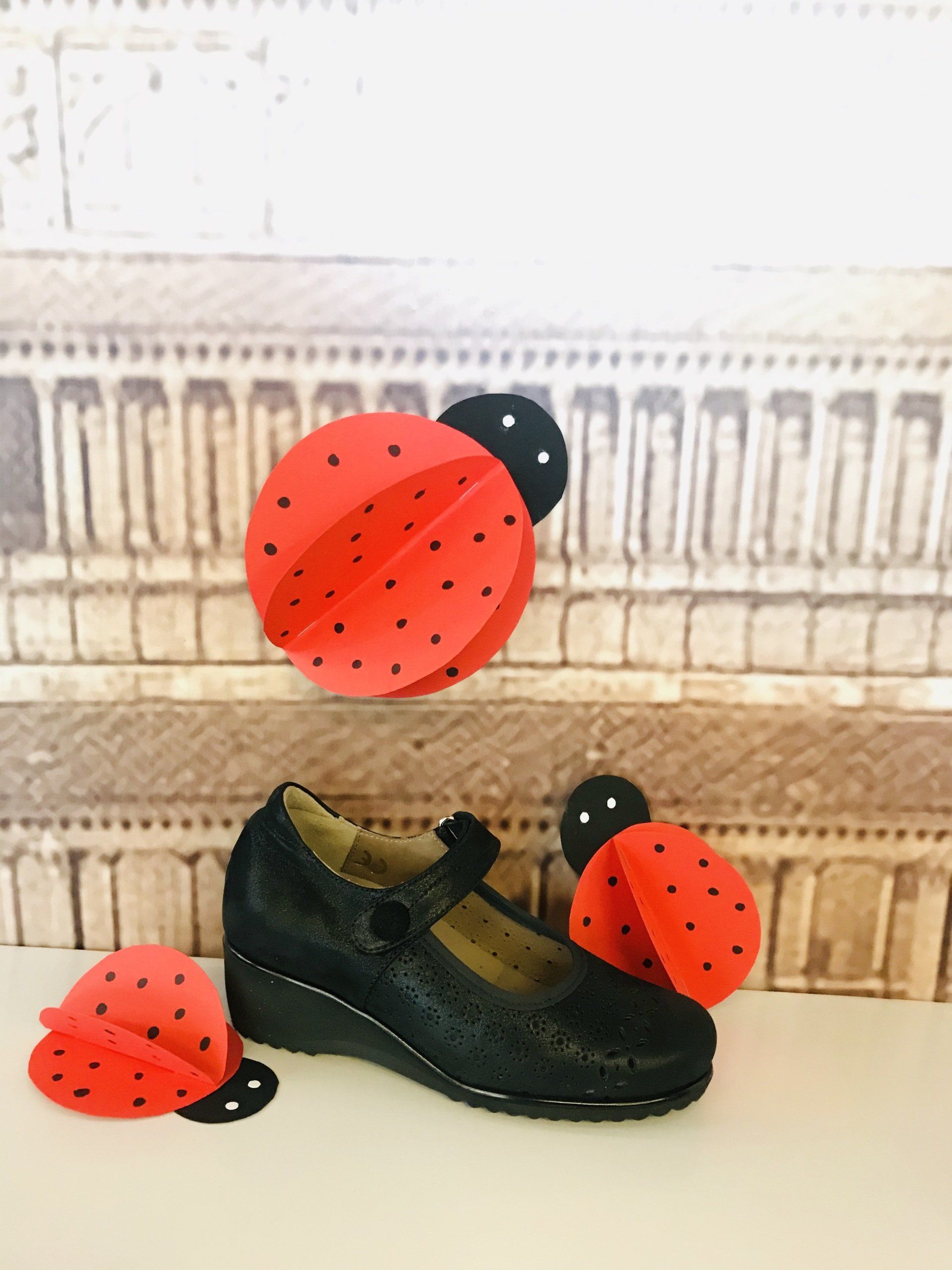 Scarpa Mary Jane nera con decorazioni a forma di coccinella su sfondo testurizzato.