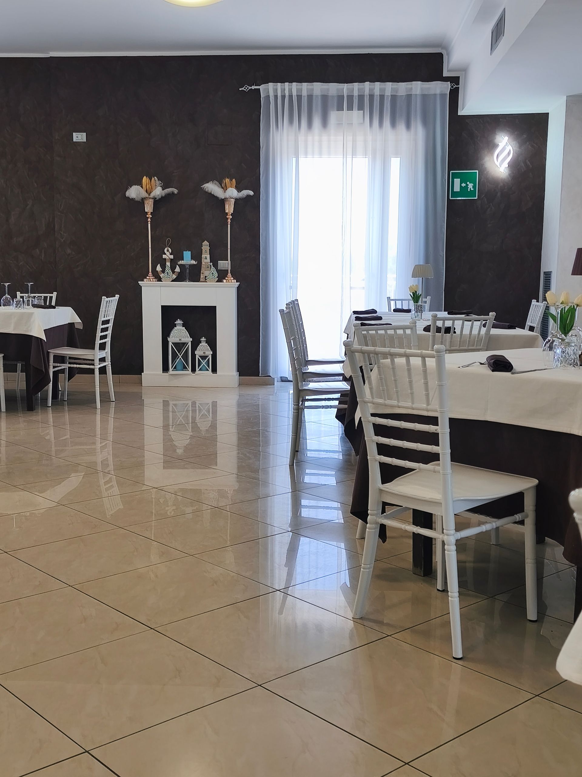 Elegante sala per banchetti con sedie bianche, tavoli rotondi e una luminosa porta finestrata.