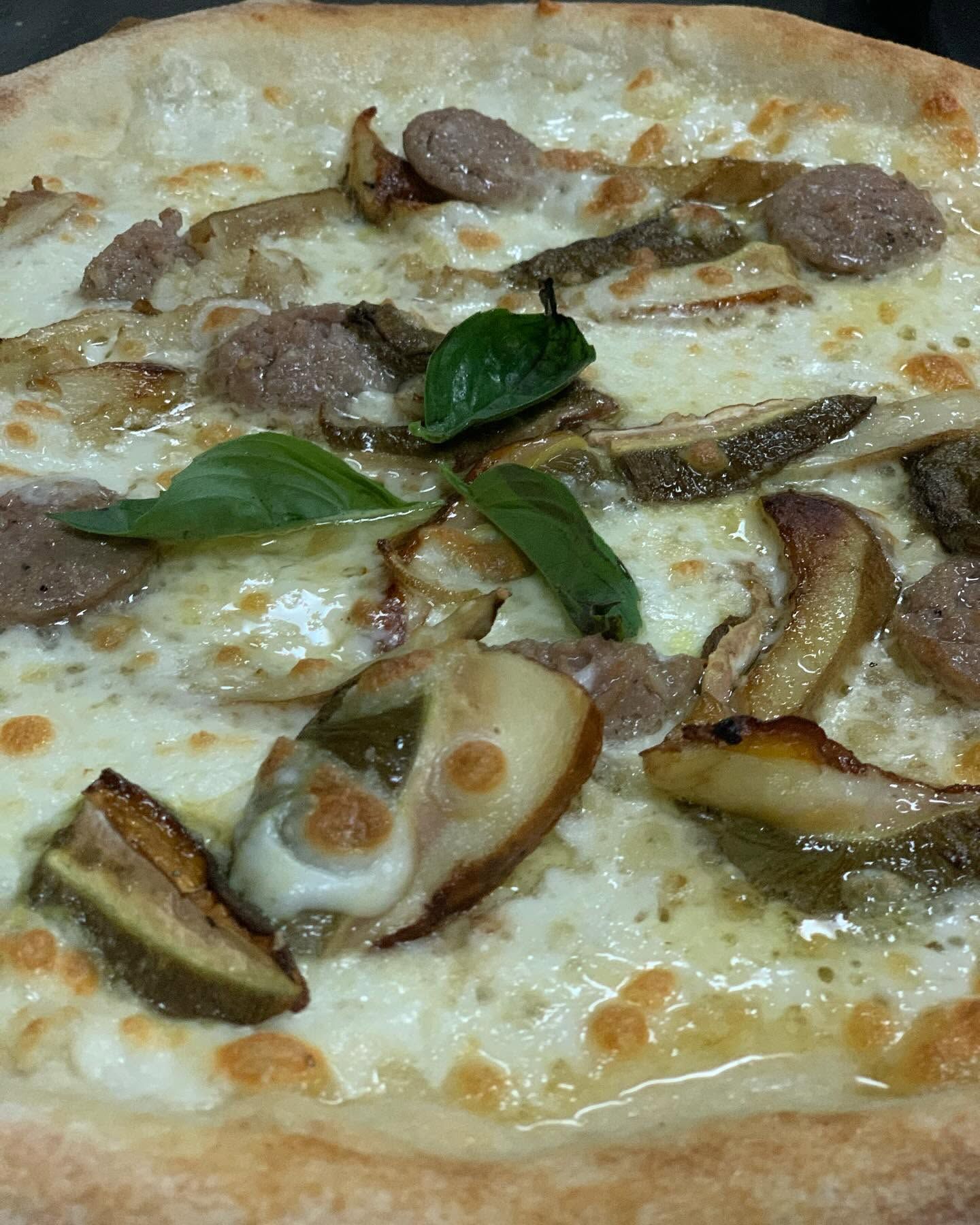 Pizza bianca condita con funghi, foglie di basilico e fette di salsiccia.