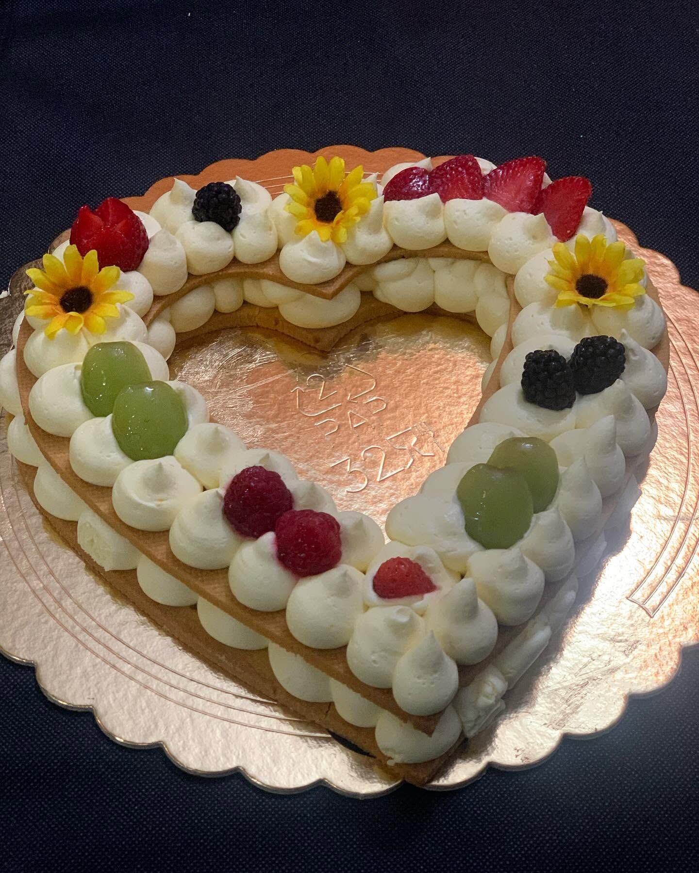 Torta a forma di cuore con crema alla frutta, guarnita con fragole, uva e fiori edibili