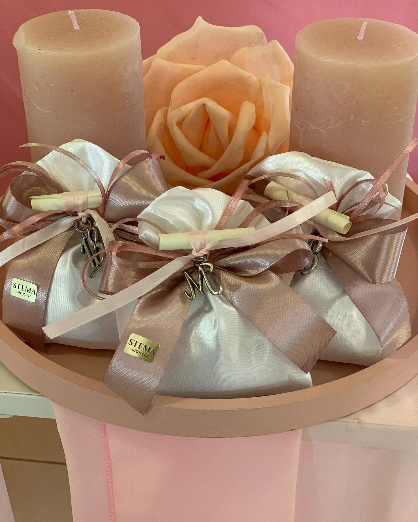 Composizione regalo rosa con due candele, un centrotavola di rose e fiocchi di nastro di raso su una scatola rotonda.
