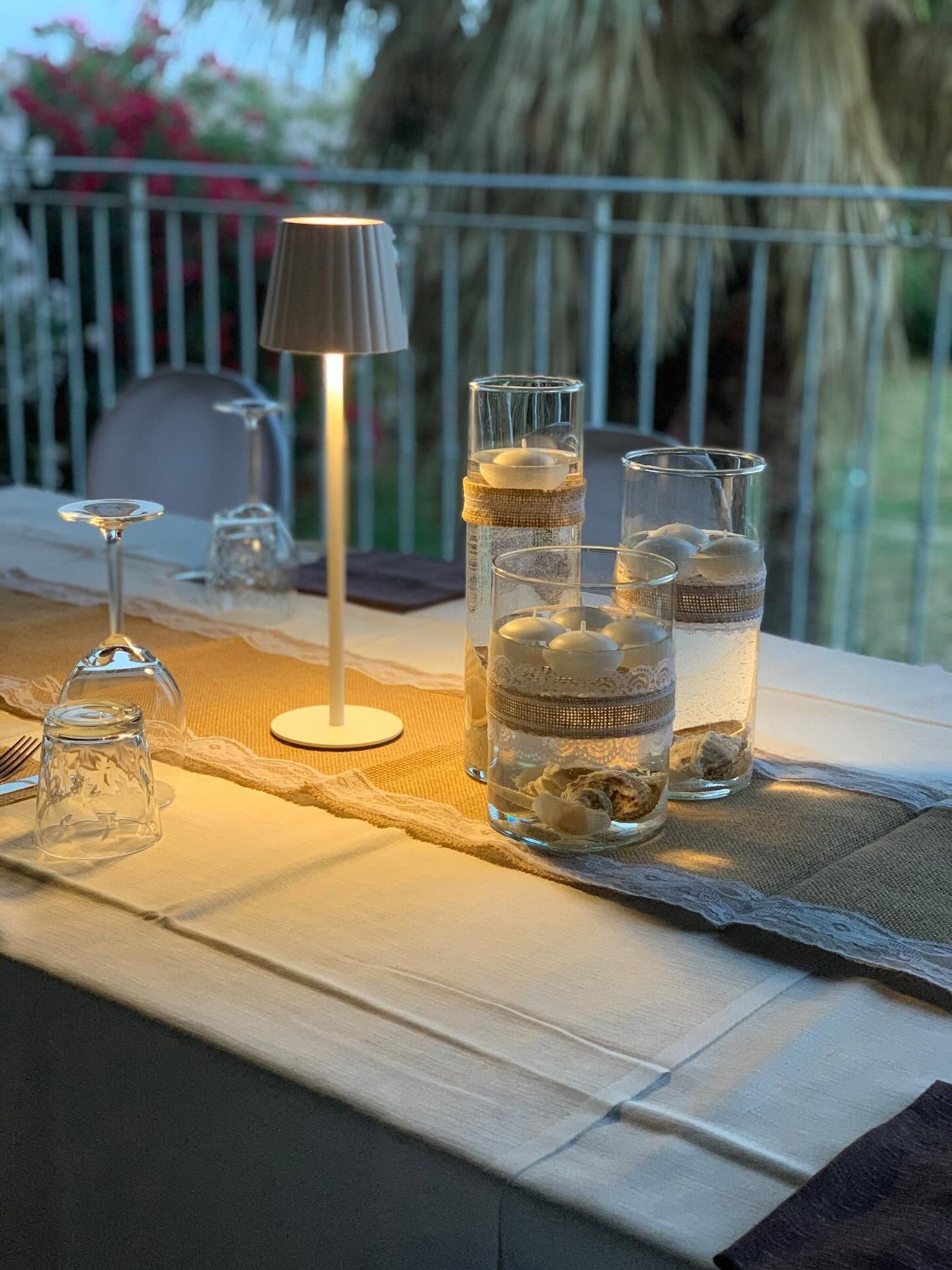 Due bicchieri e una bottiglia su un tavolo illuminato da una piccola lampada al crepuscolo su un balcone.