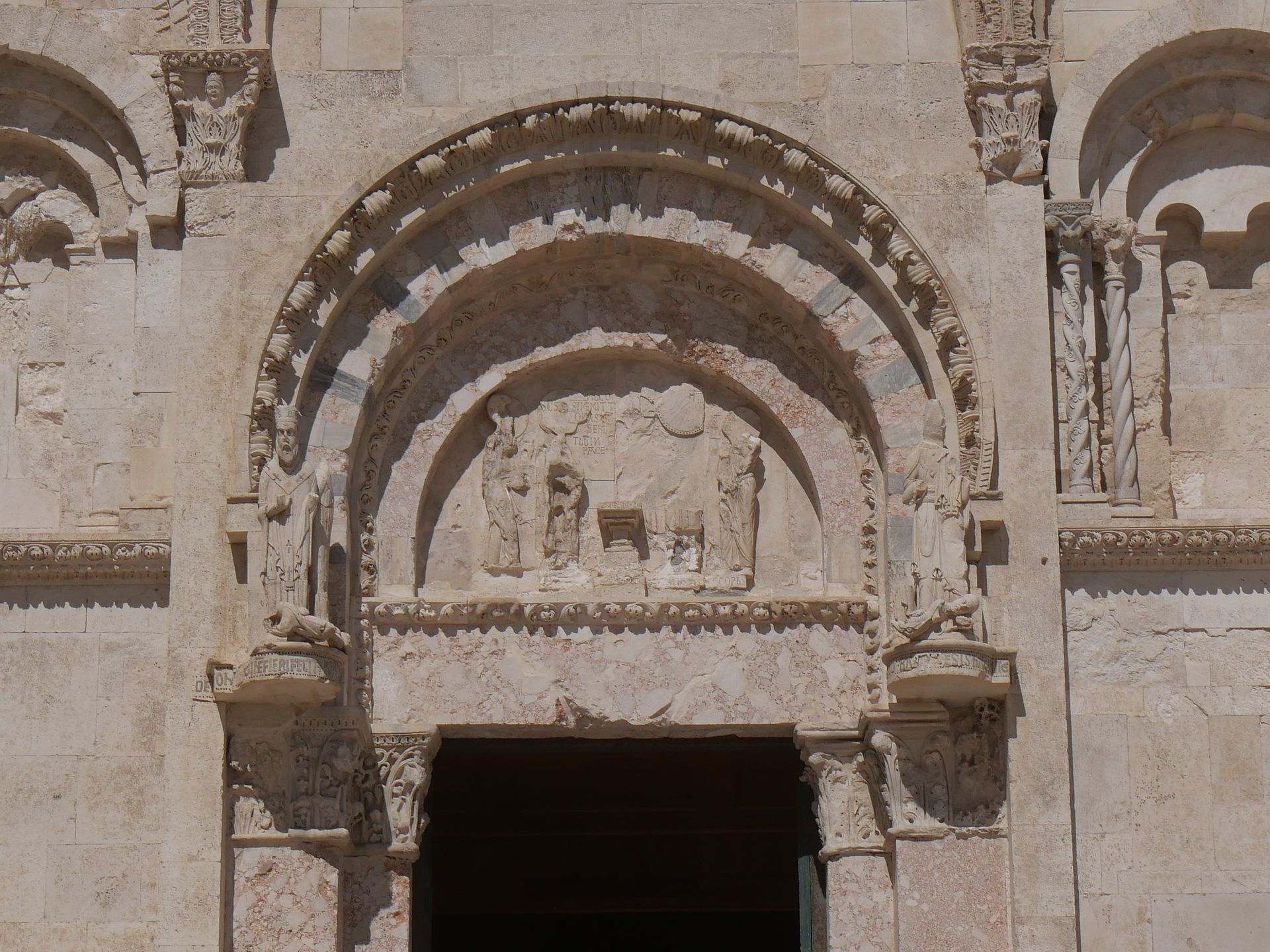 Arco in pietra scolpita sopra un portale scuro sulla facciata riccamente decorata di un edificio storico.