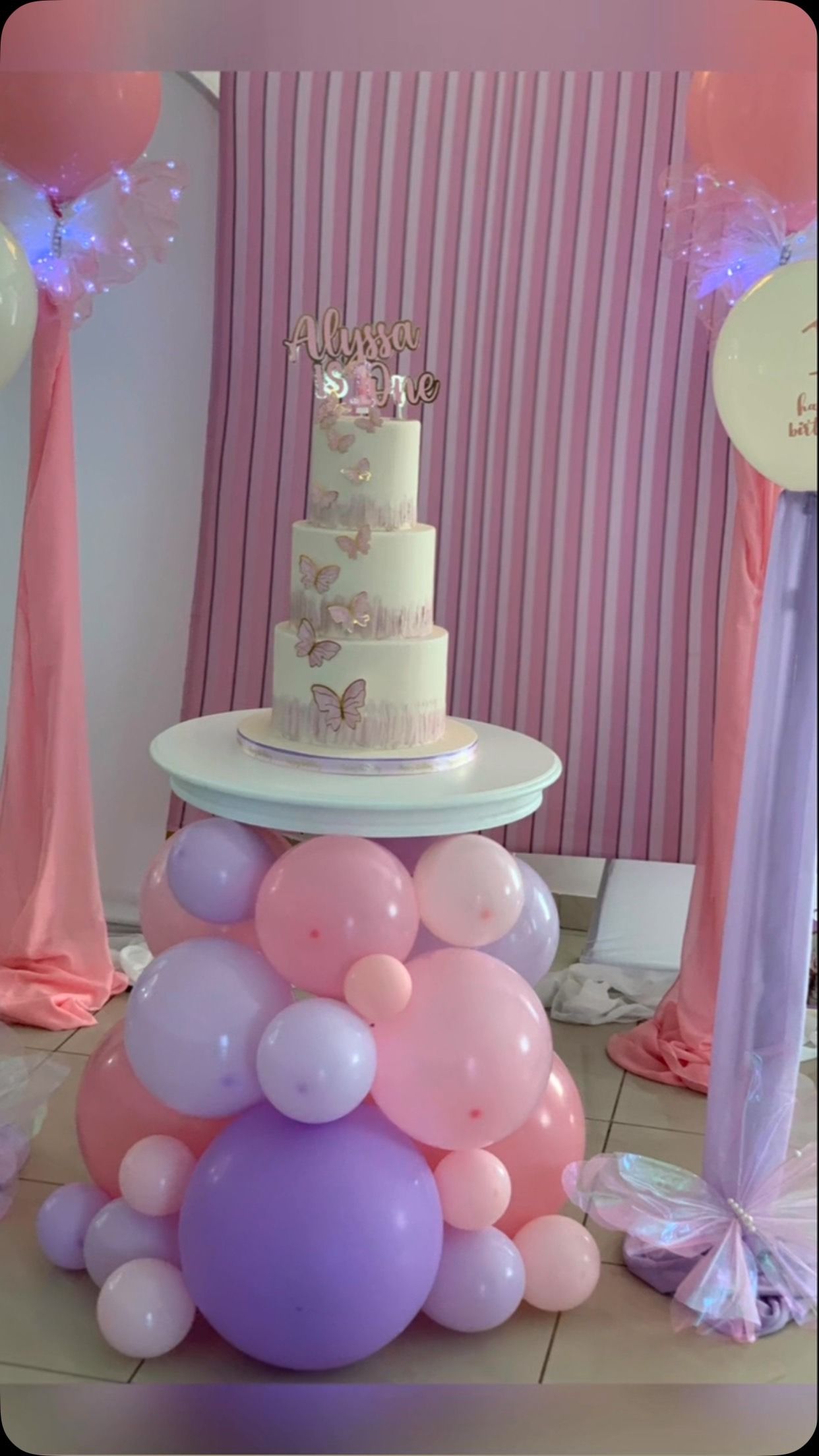 Composizione di palloncini color pastello con una torta a più piani, sullo sfondo di drappeggi rosa.