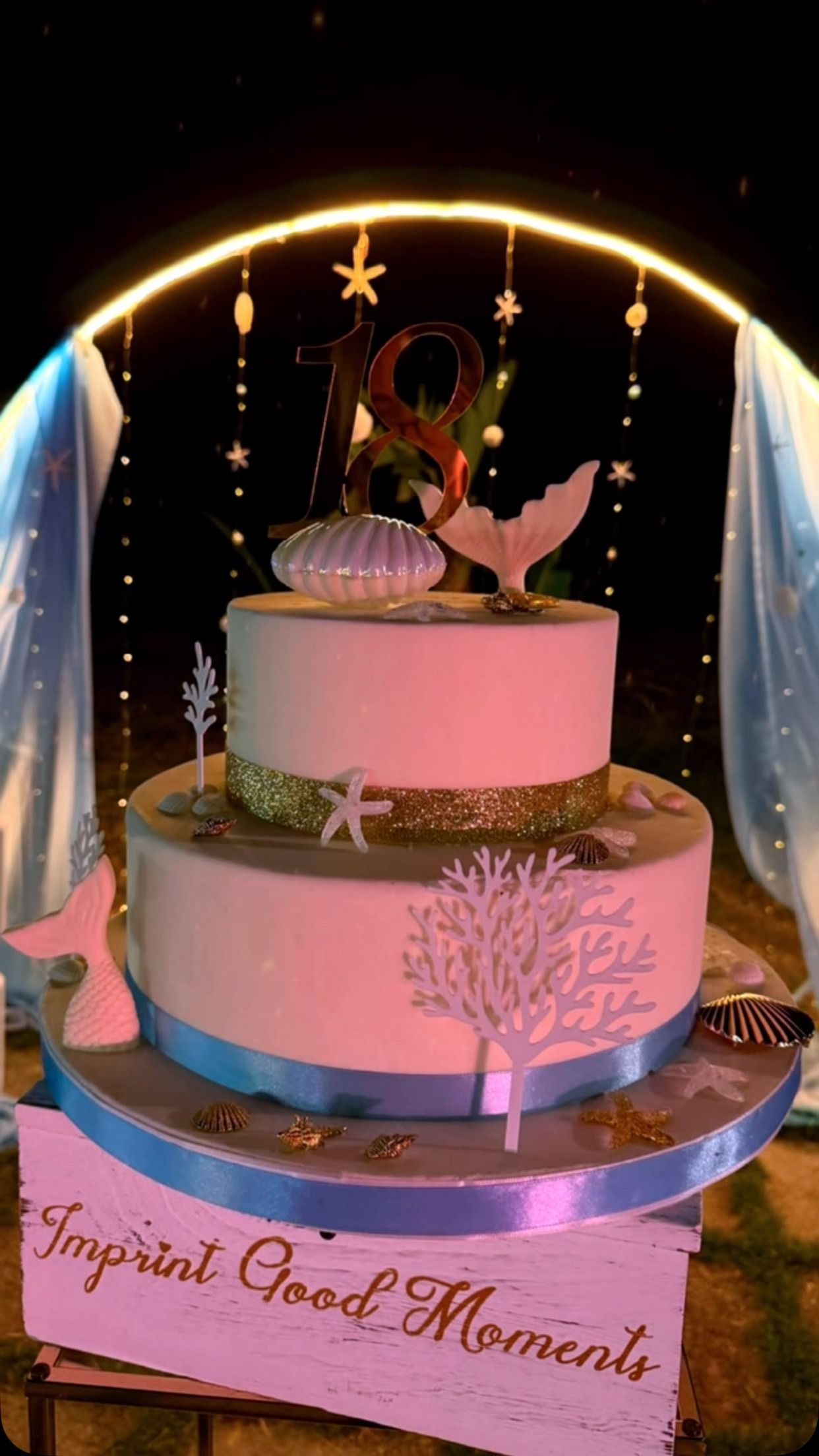 Torta rosa a due piani sotto un arco illuminato, decorata con fiori e dettagli dorati