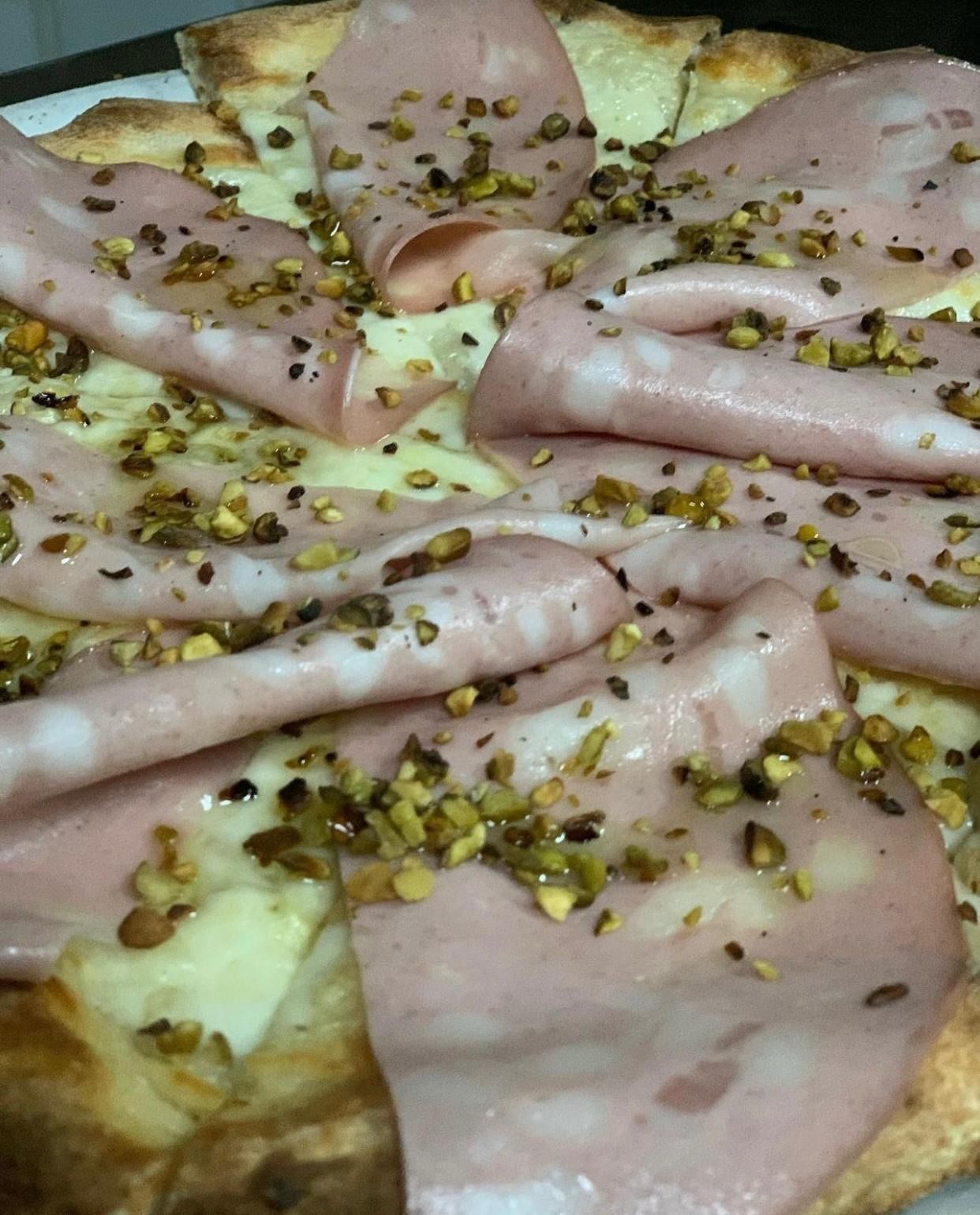 Pizza condita con fette di prosciutto piegate e pistacchi tritati su una base cotta al forno
