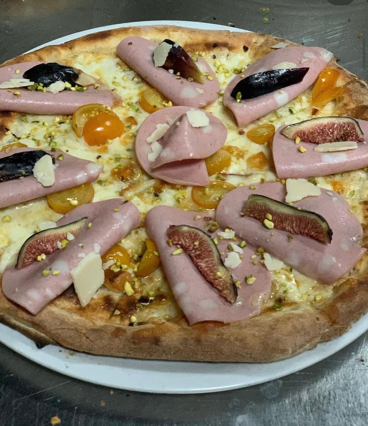Pizza condita con fette di prosciutto, olive, pomodorini e formaggio