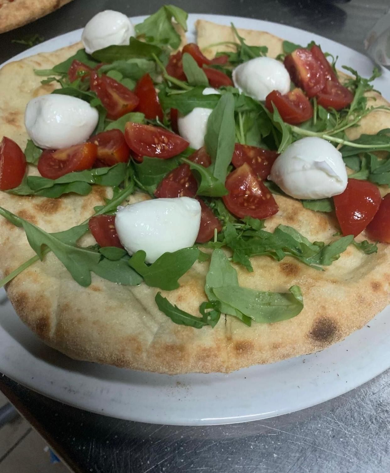 Pizza su pane piatto con rucola, pomodori e mozzarella, servita su un piatto bianco.