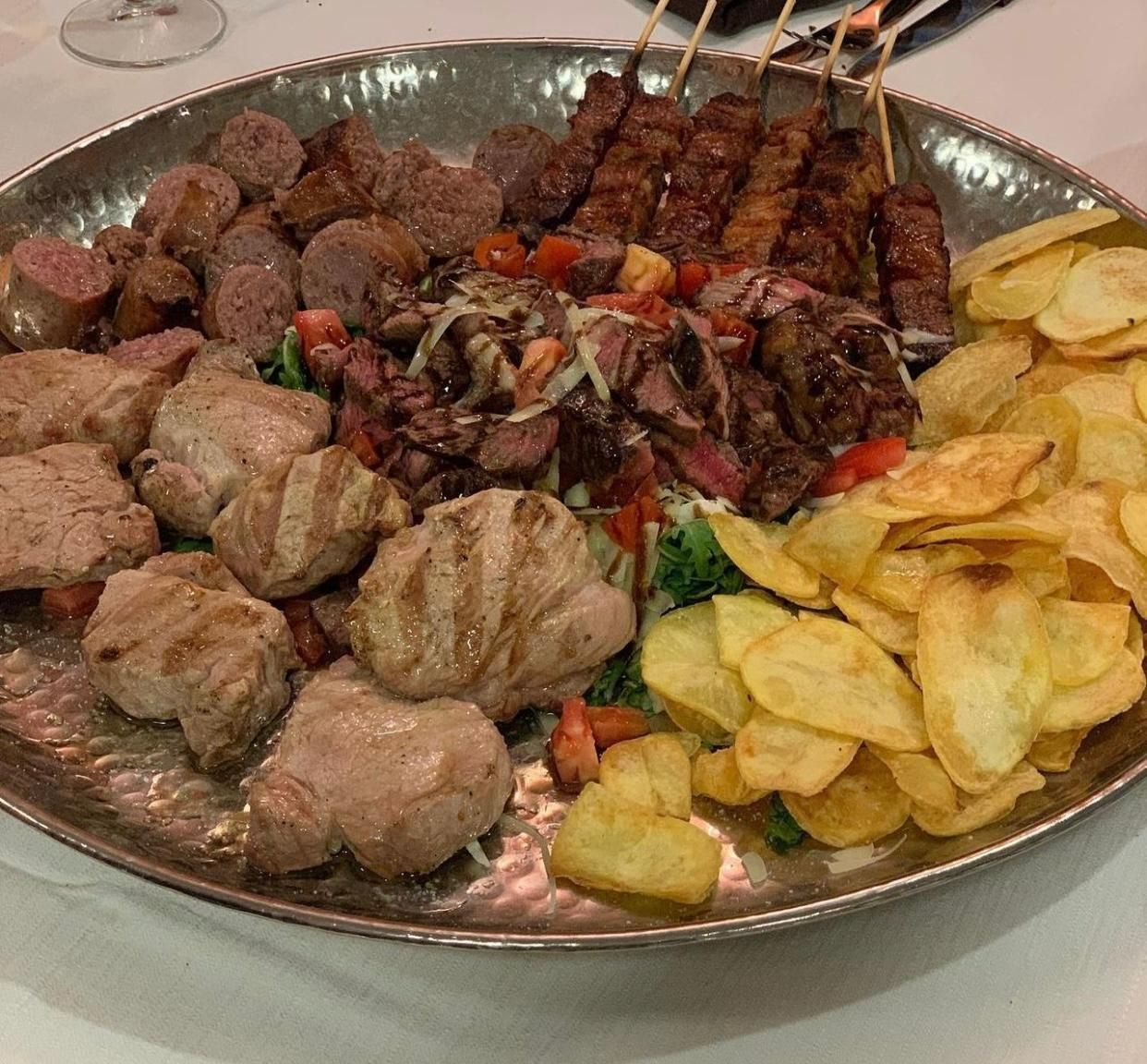 Un grande piatto con un assortimento di carni grigliate e salsicce, accompagnato da patatine fritte