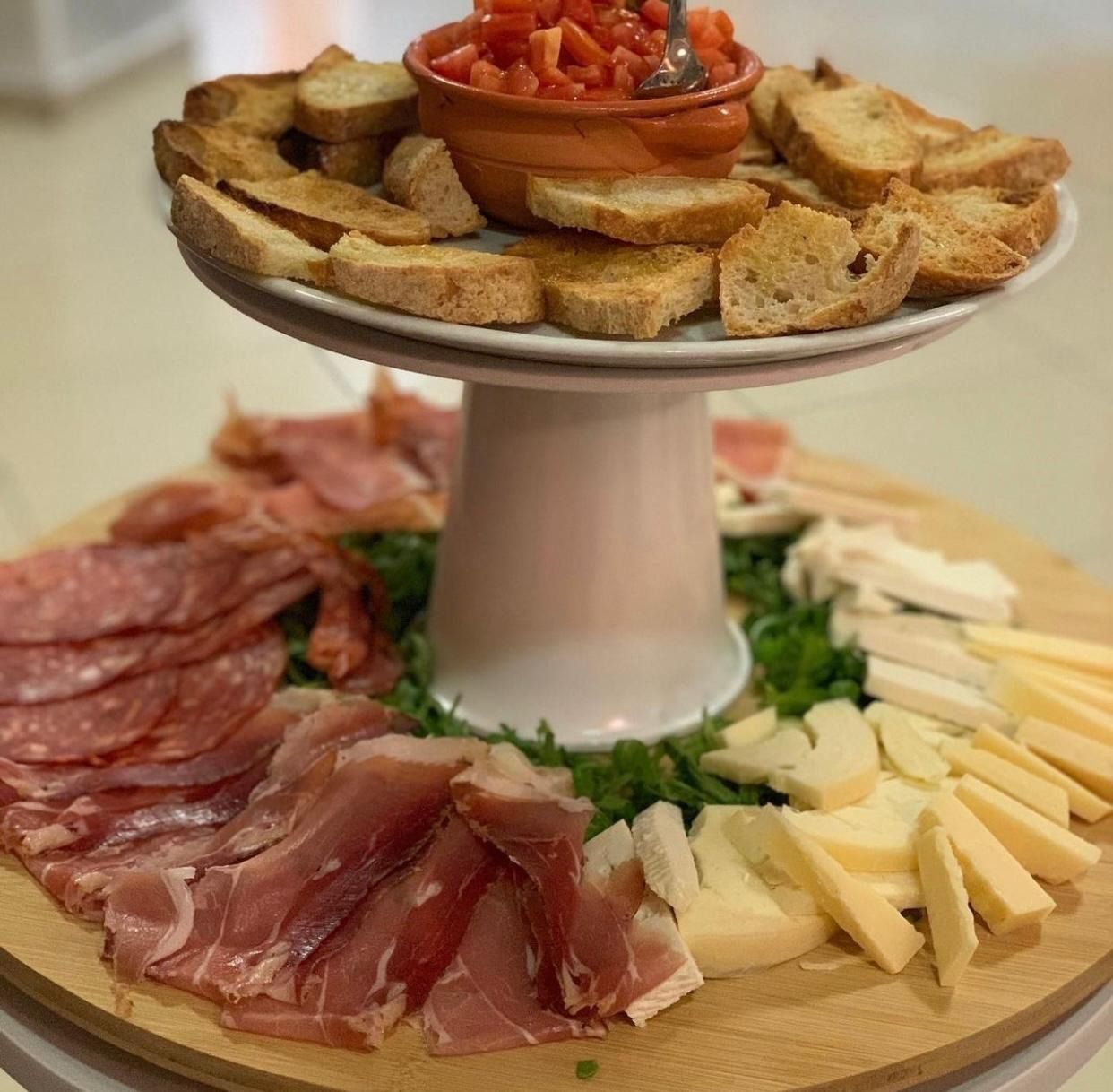 Piatto da portata a più livelli con pane, salsa di pomodoro, salumi, formaggio e crostini.