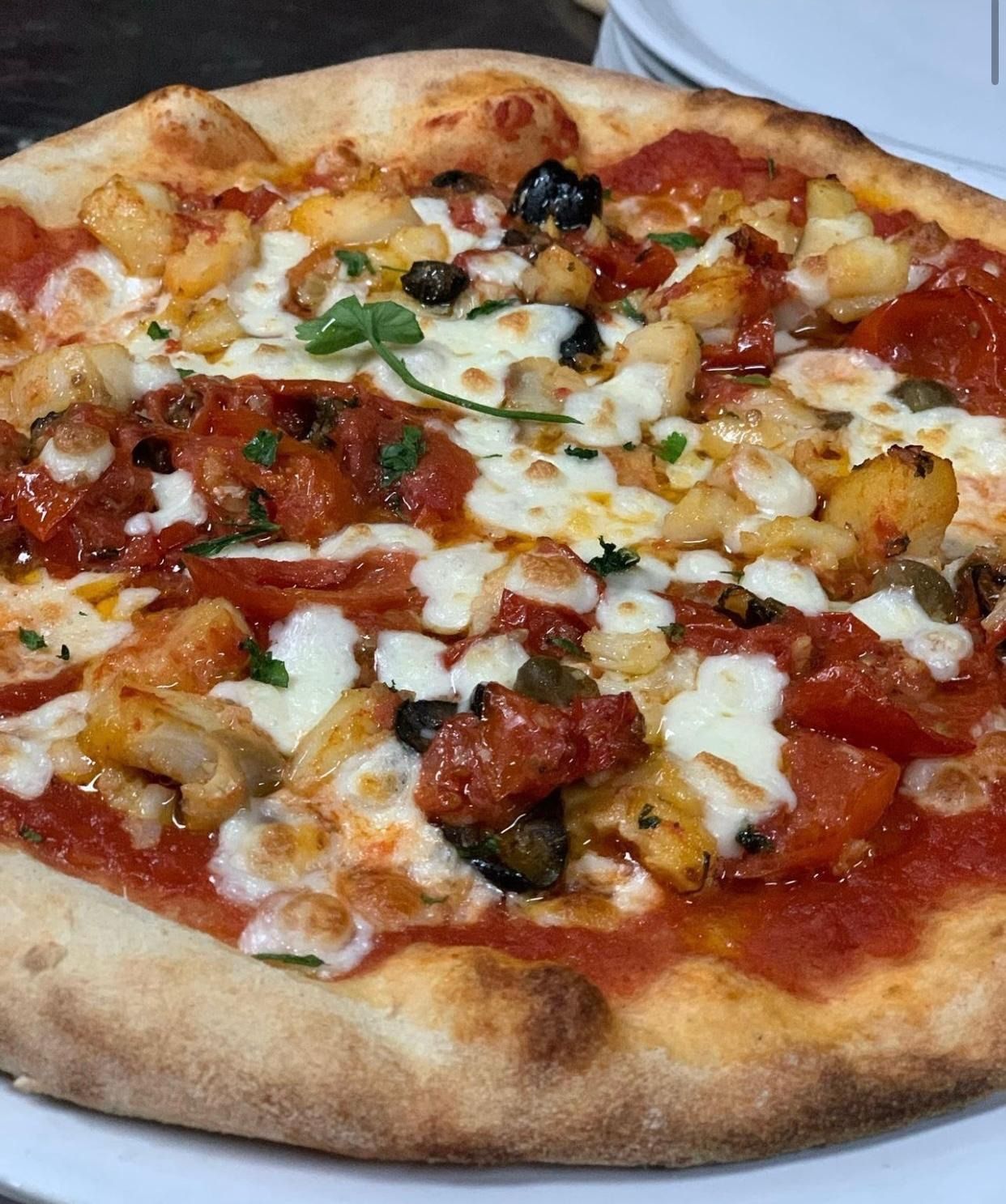 Primo piano di una pizza con formaggio e verdure, salsa di pomodoro e crosta dorata.