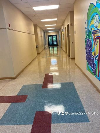 Empty school hallway with beige walls, tiled floor, and colorful mural on the right wall