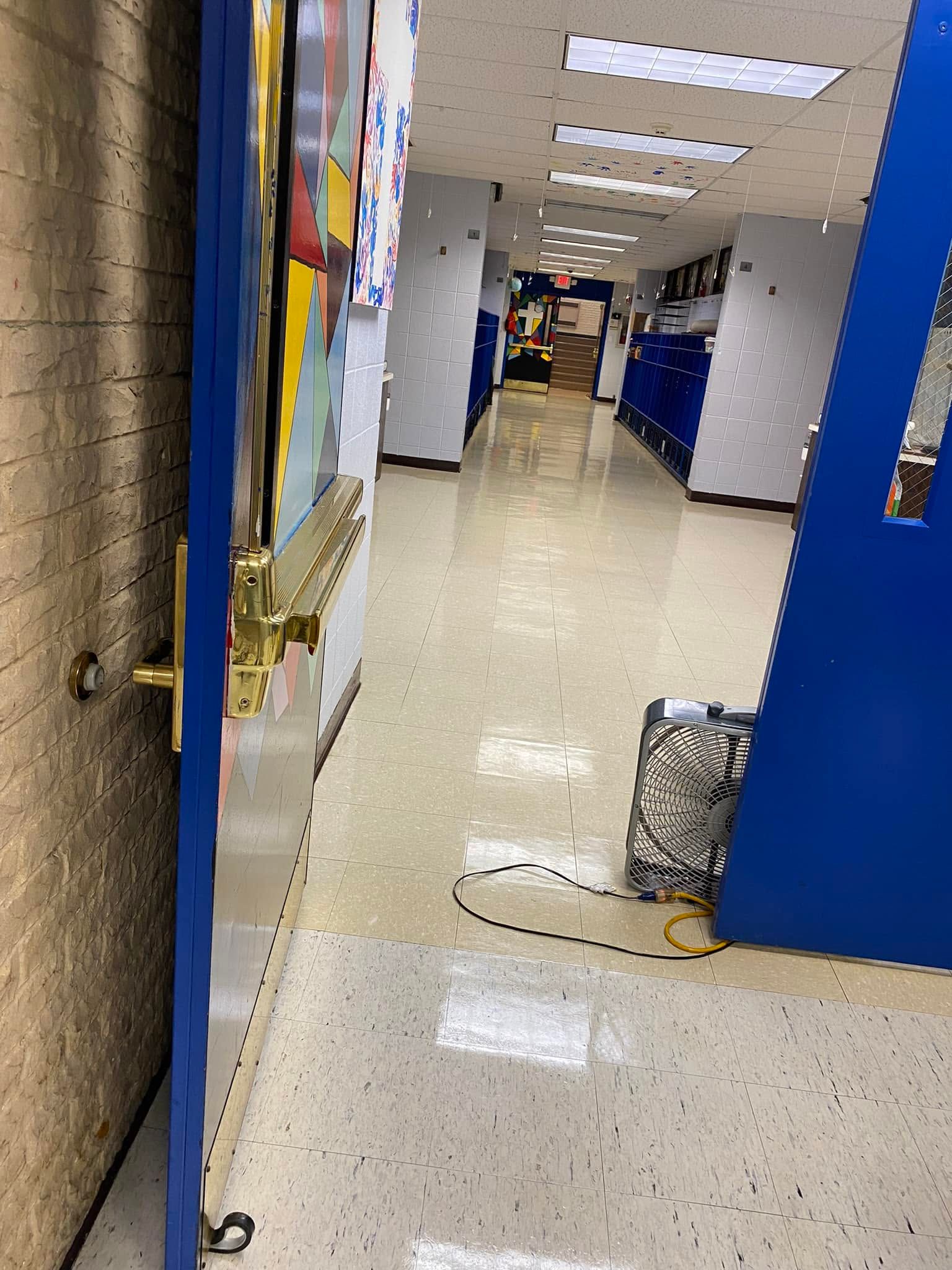 School hallway with blue lockers and a door open to the corridor.