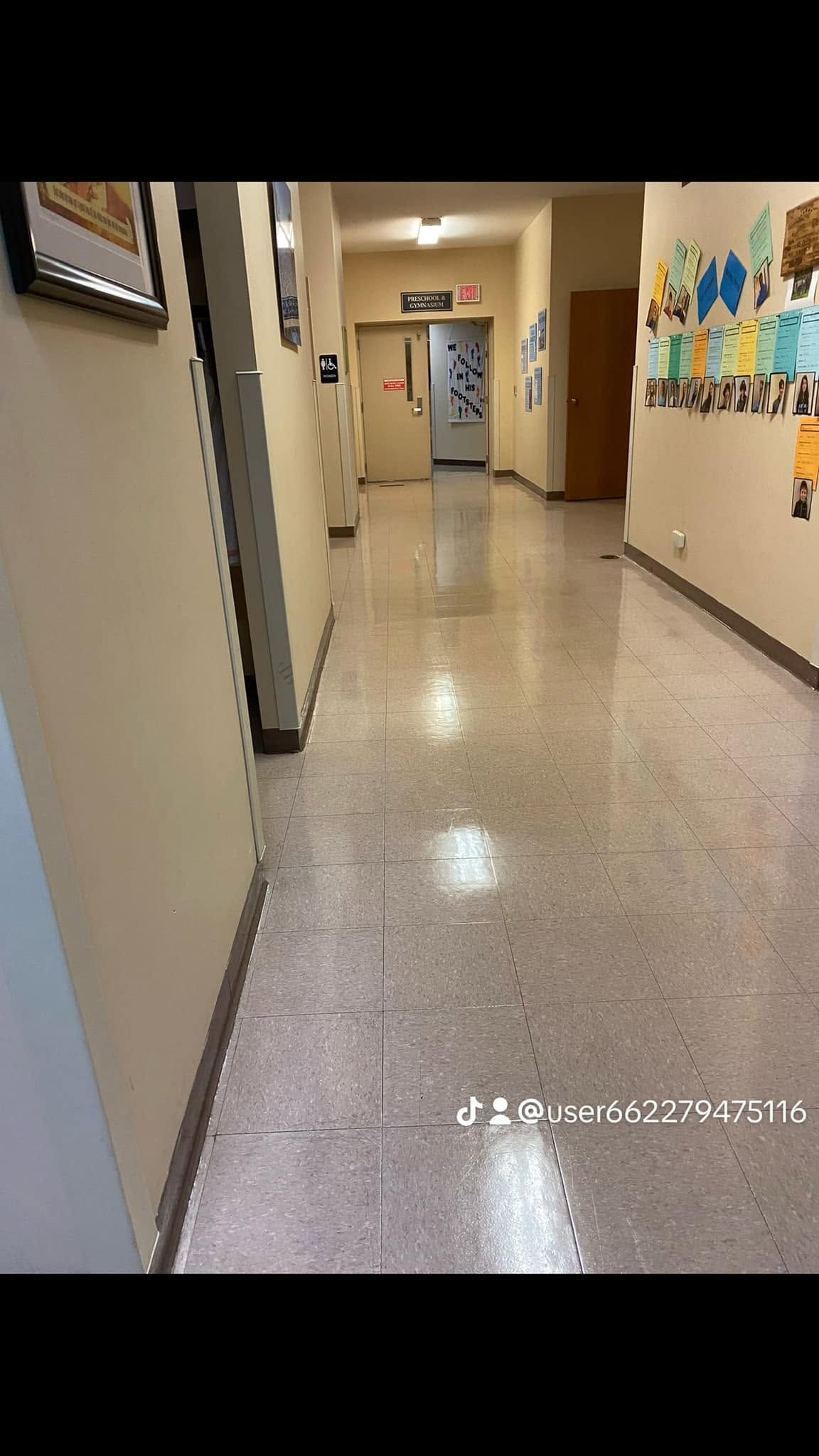 Empty school hallway with beige walls, colorful student artwork, and glossy speckled floor.