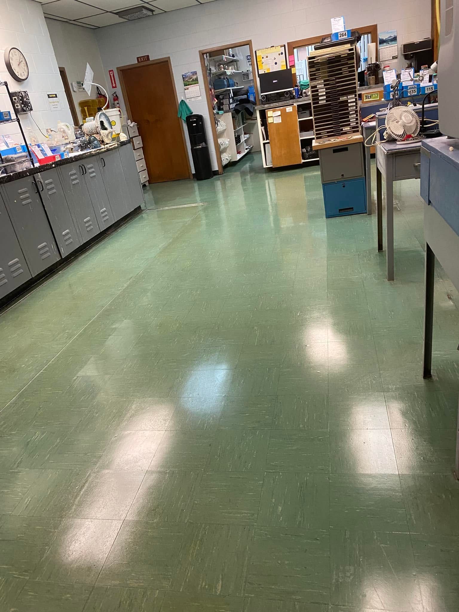 Empty laboratory room with green floor, cabinets, tables, and equipment along the walls