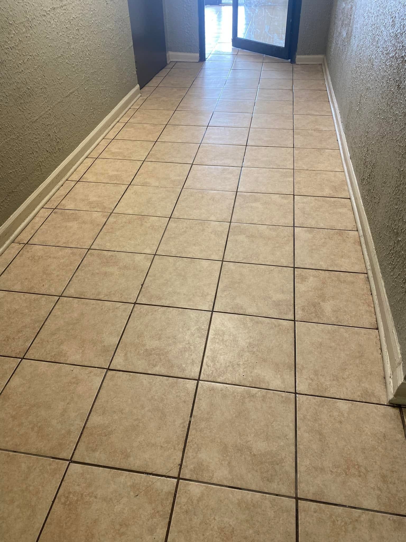 Narrow tiled hallway with beige walls and an open doorway at the end.