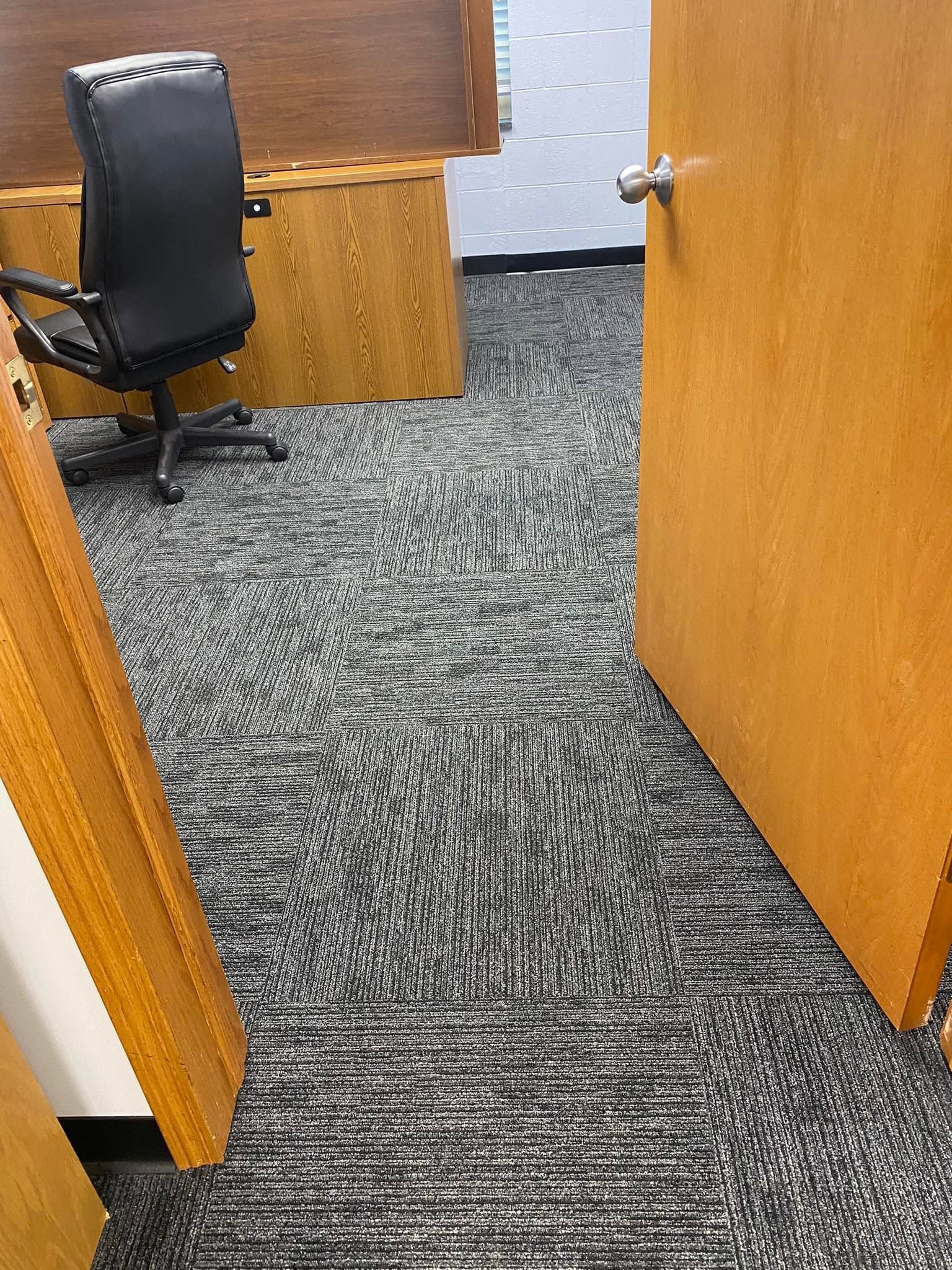 Office doorway with wood-paneled walls, gray carpet, and a black rolling chair inside