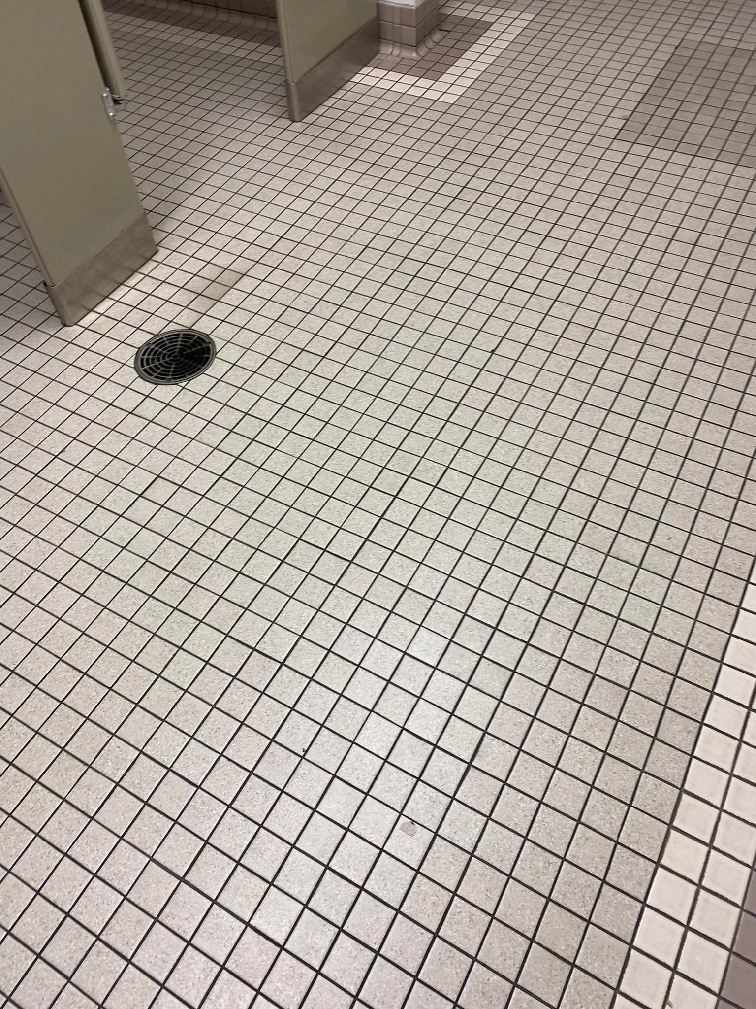 Tiled bathroom floor with a floor drain and a partial stall wall.