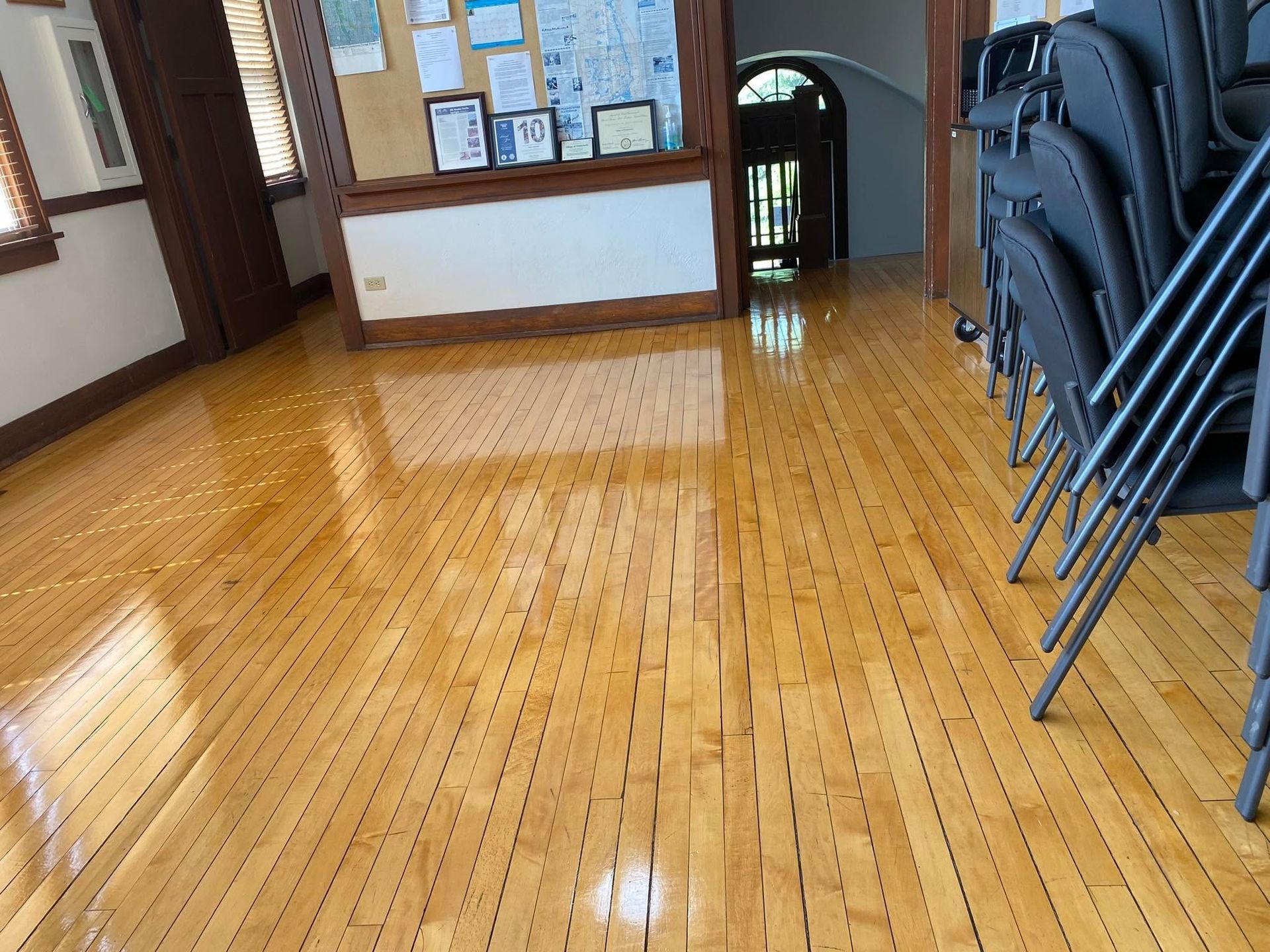 Empty polished wooden floor in a room with stacked chairs along the right wall.