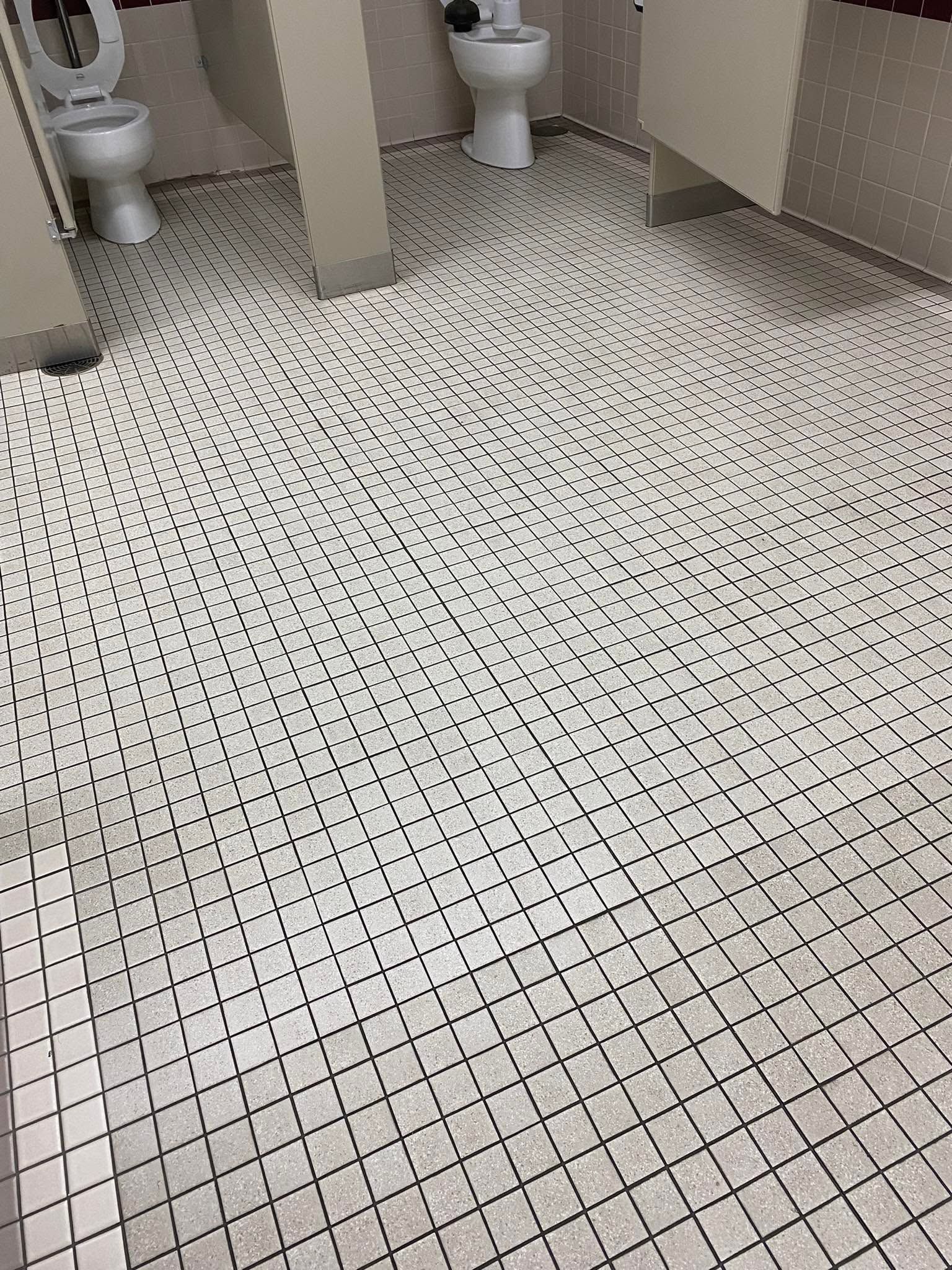 Tiled restroom floor with white and black mosaic tiles, showing two toilets at the top edge.