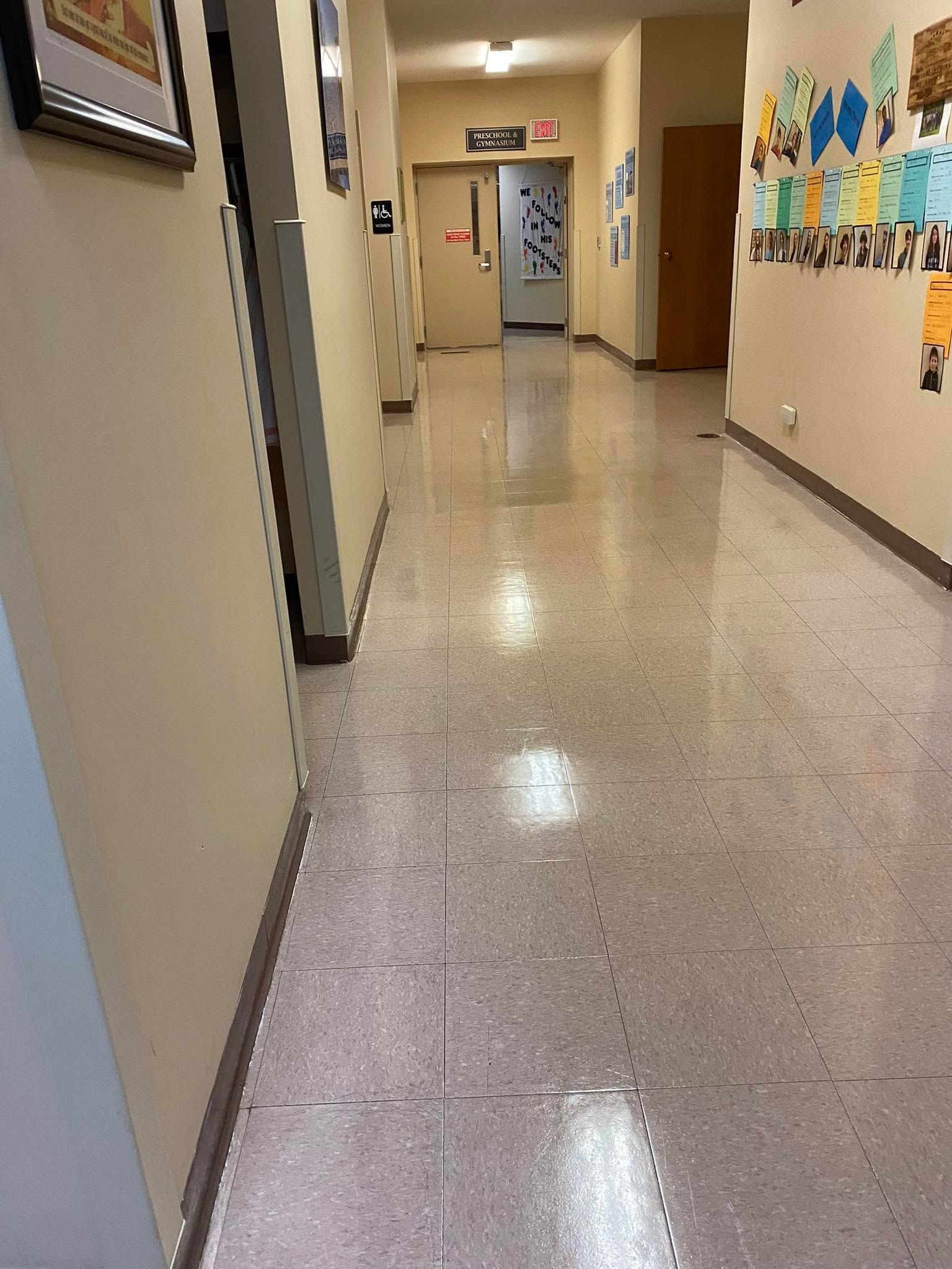 Empty school hallway with beige walls, glossy floor, and classroom doors along the corridor