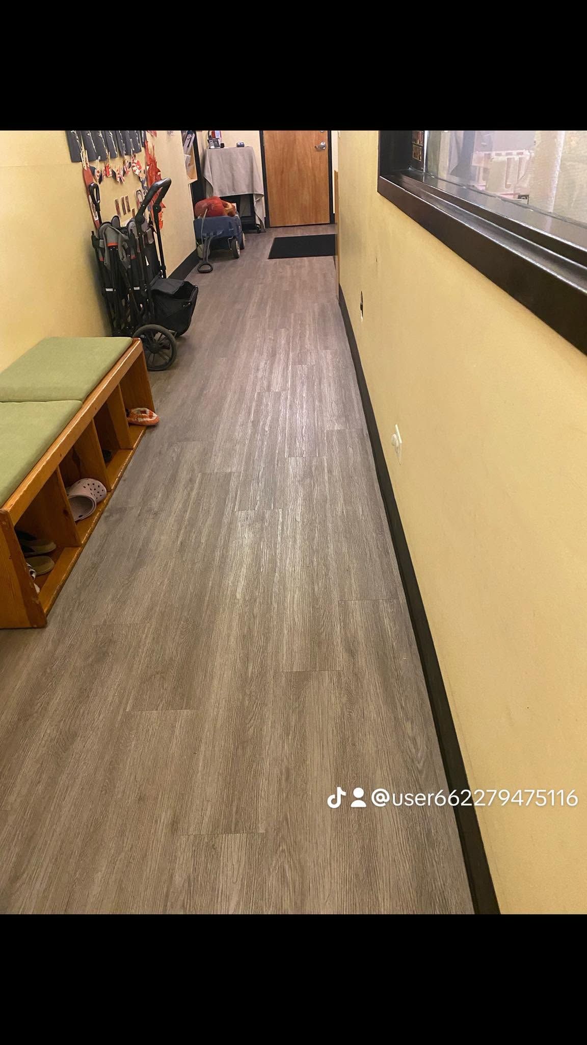 Long narrow hallway with yellow walls, a bench on the left, and a windowed wall on the right.