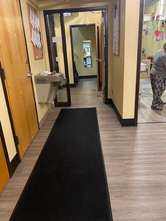 Hallway with black runner, beige walls, water fountain, and a person standing near an open doorway.