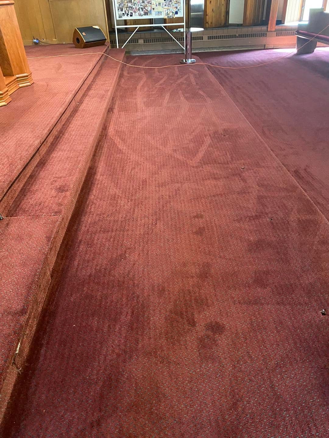 Maroon carpeted aisle in a room, with a few chairs and furniture at the far end.