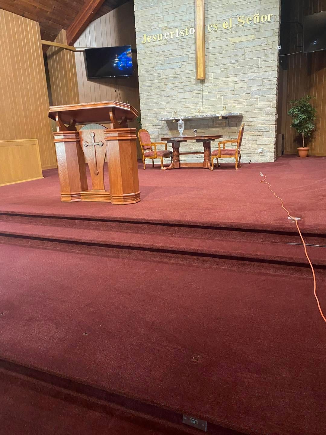 Church stage with pulpit, chairs, and red carpeted steps under warm lighting
