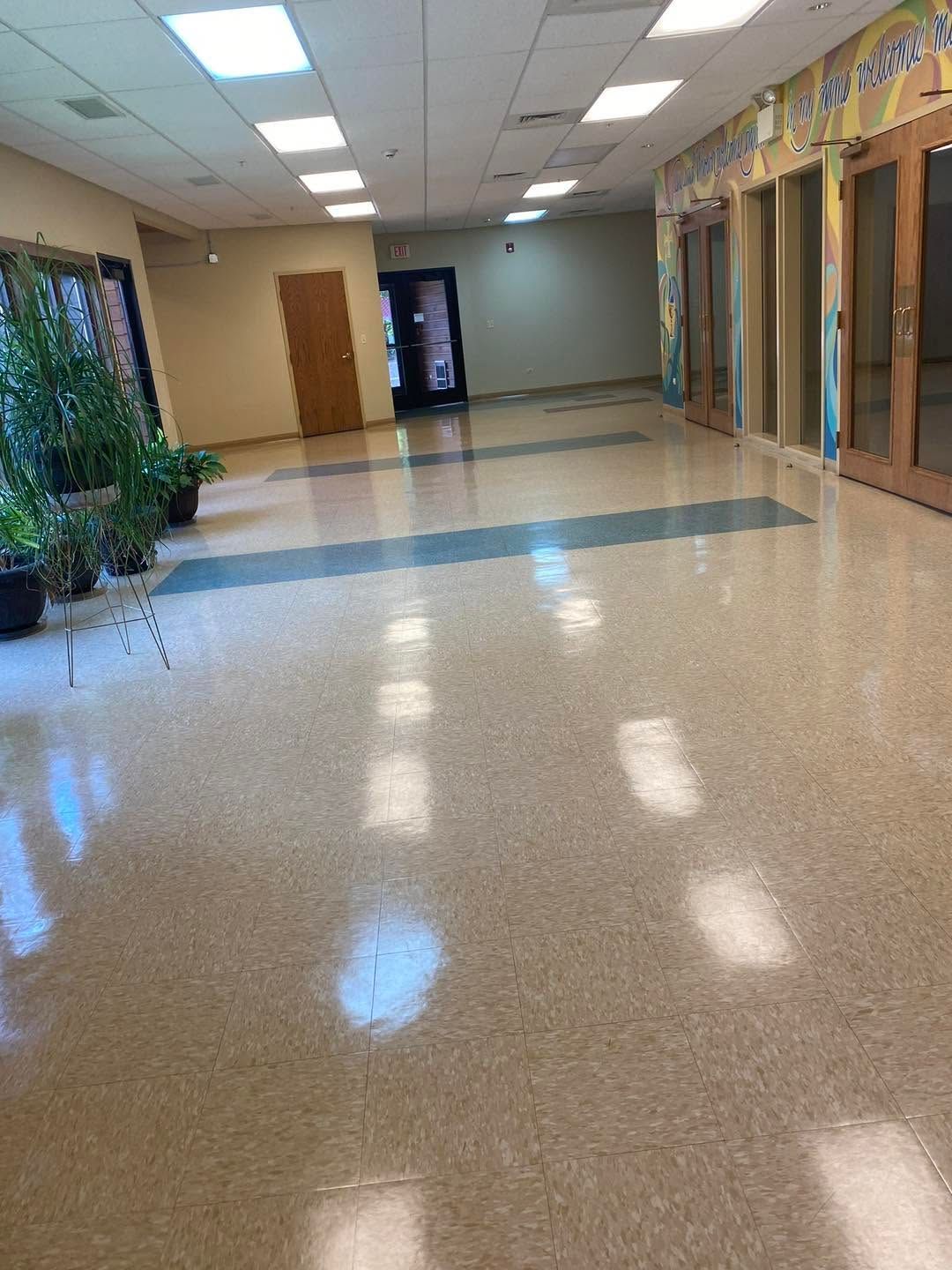 Empty school hallway with glossy tile floor, ceiling lights, doors, and windows along the right wall