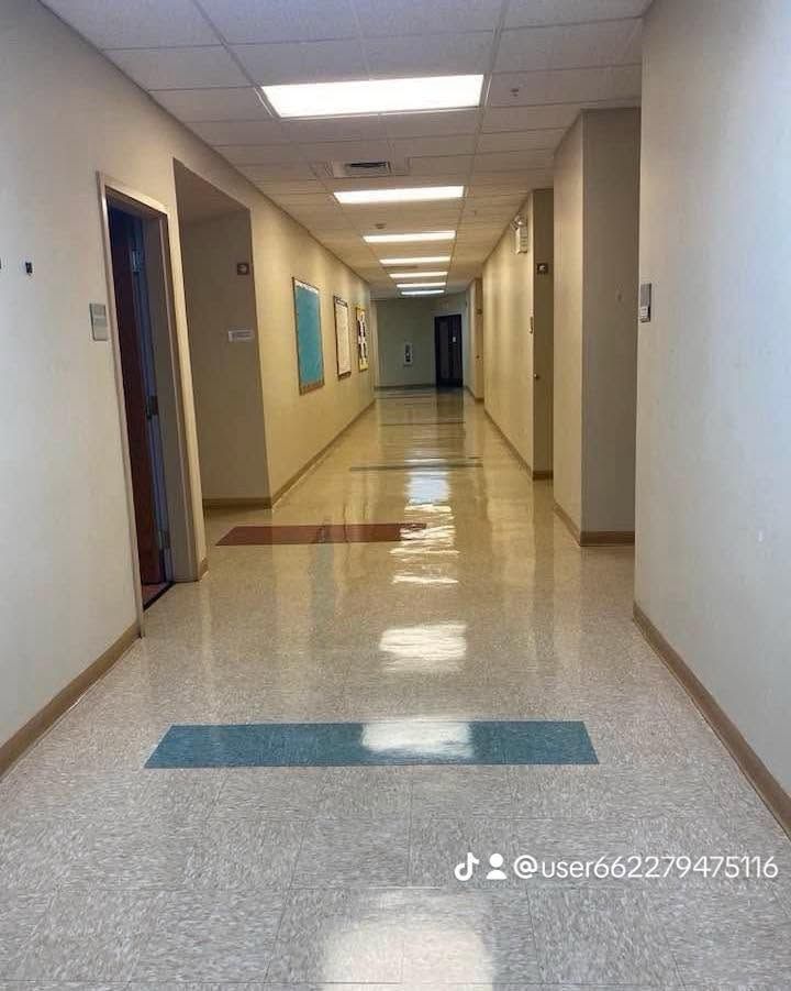 Empty indoor hallway with beige walls, glossy floor, blue doorways, and ceiling lights